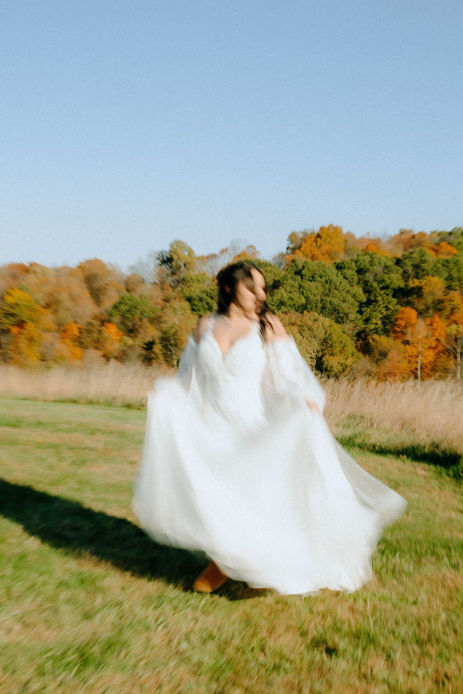 Bride twirling in flowing white dress against autumn landscape backdrop.