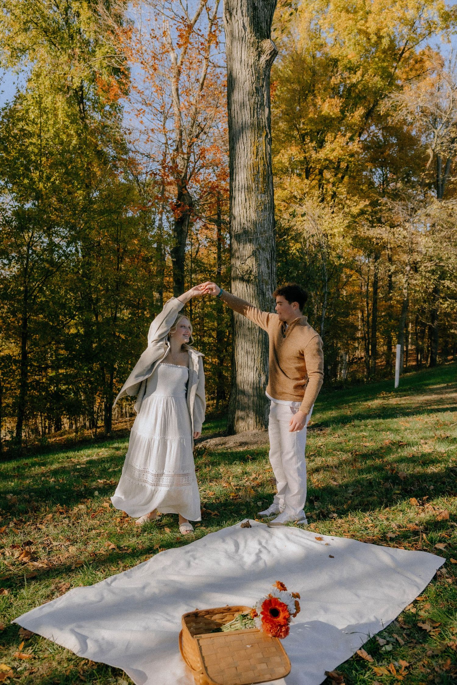 White picnic blanket laid out in a sunlit forest with golden fall foliage and a rustic basket.
