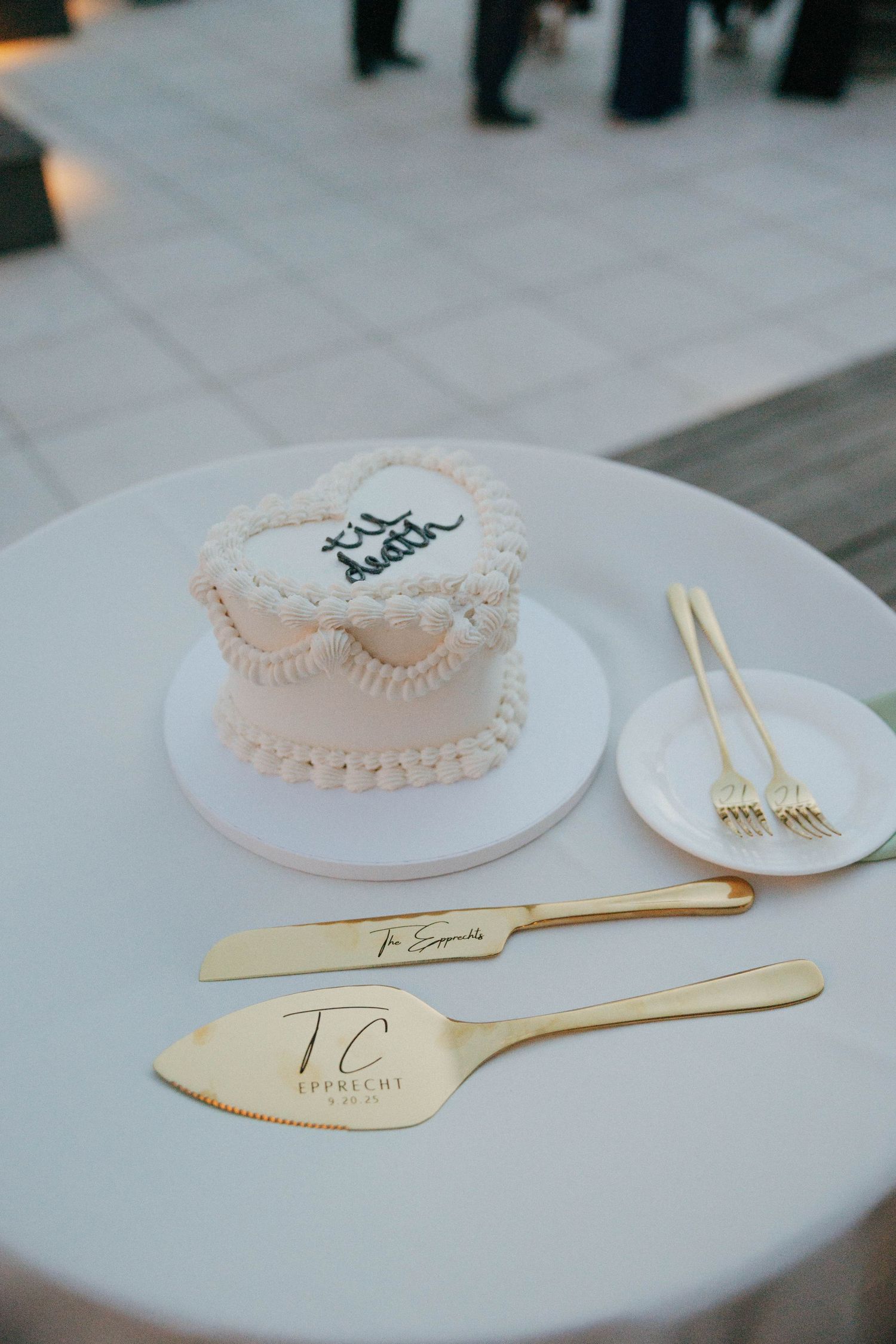 Elegant white mini wedding cake with gold serving utensils on white table.