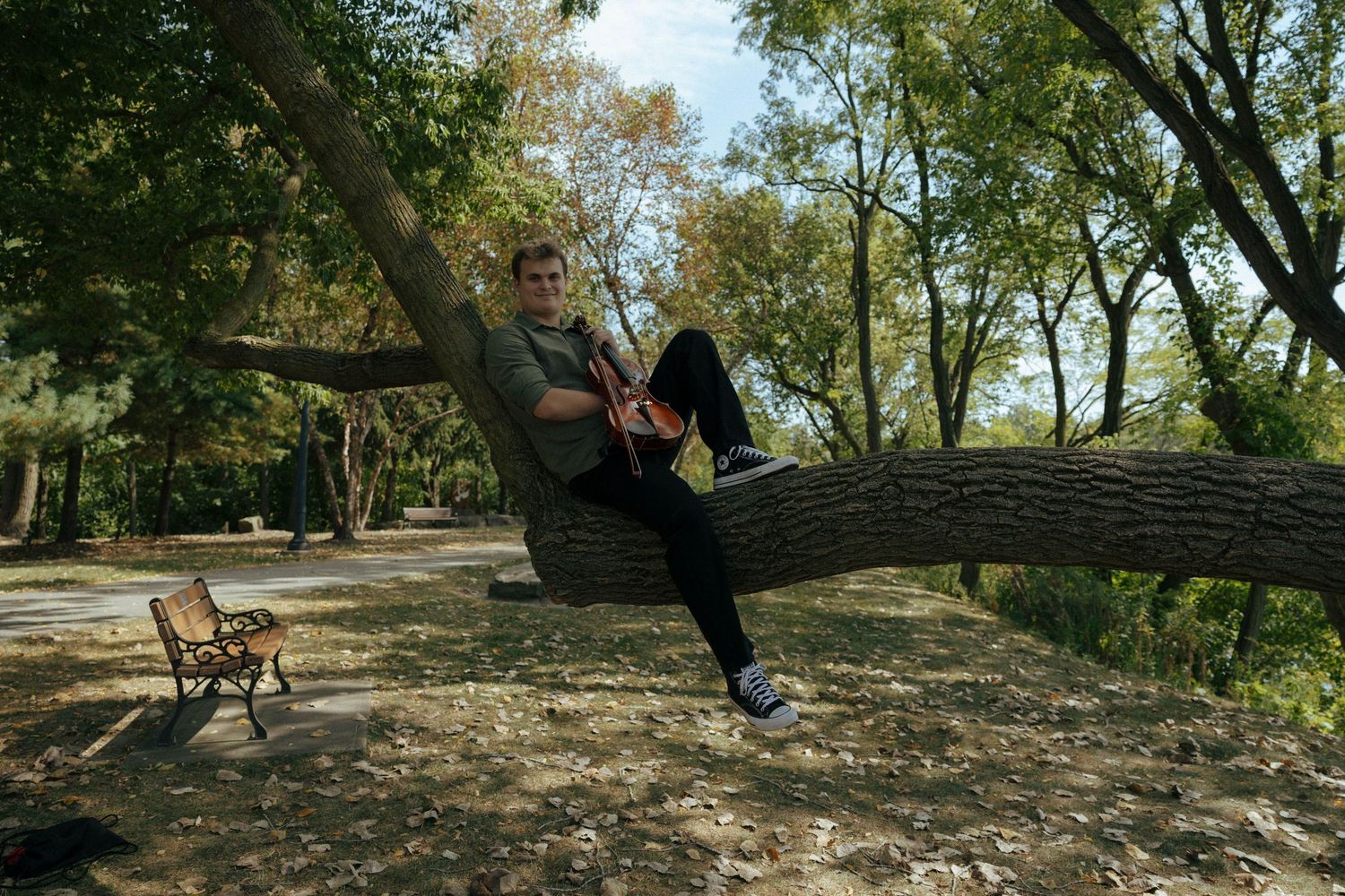 Person relaxing on a fallen tree trunk in a sunlit wooded area.