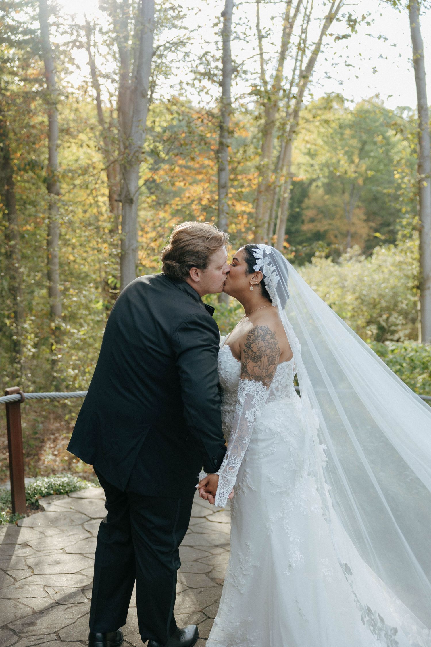 Wedding couple shares intimate moment on stone pathway surrounded by autumn trees.