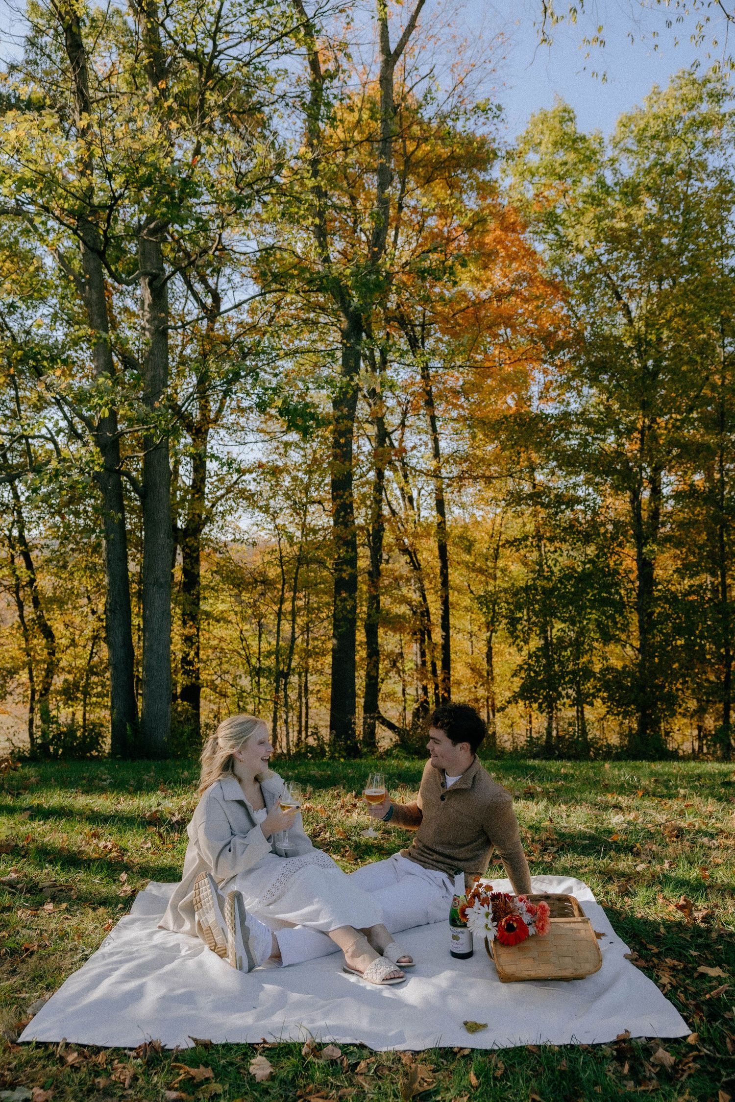 Picnic scene in a forest clearing with autumn trees and a white blanket spread on the ground.
