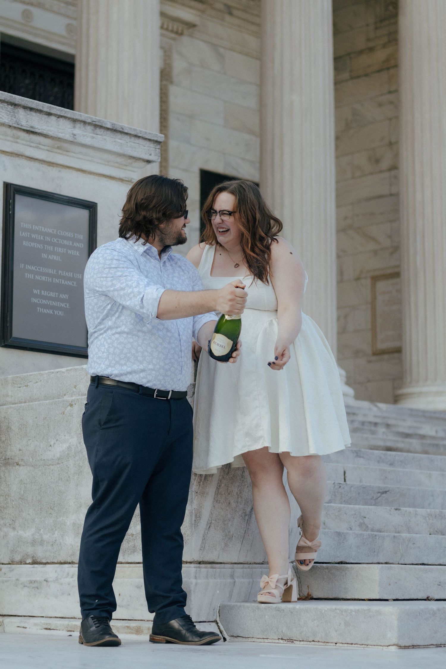 A couple shares a celebratory moment on marble steps with classical columns.