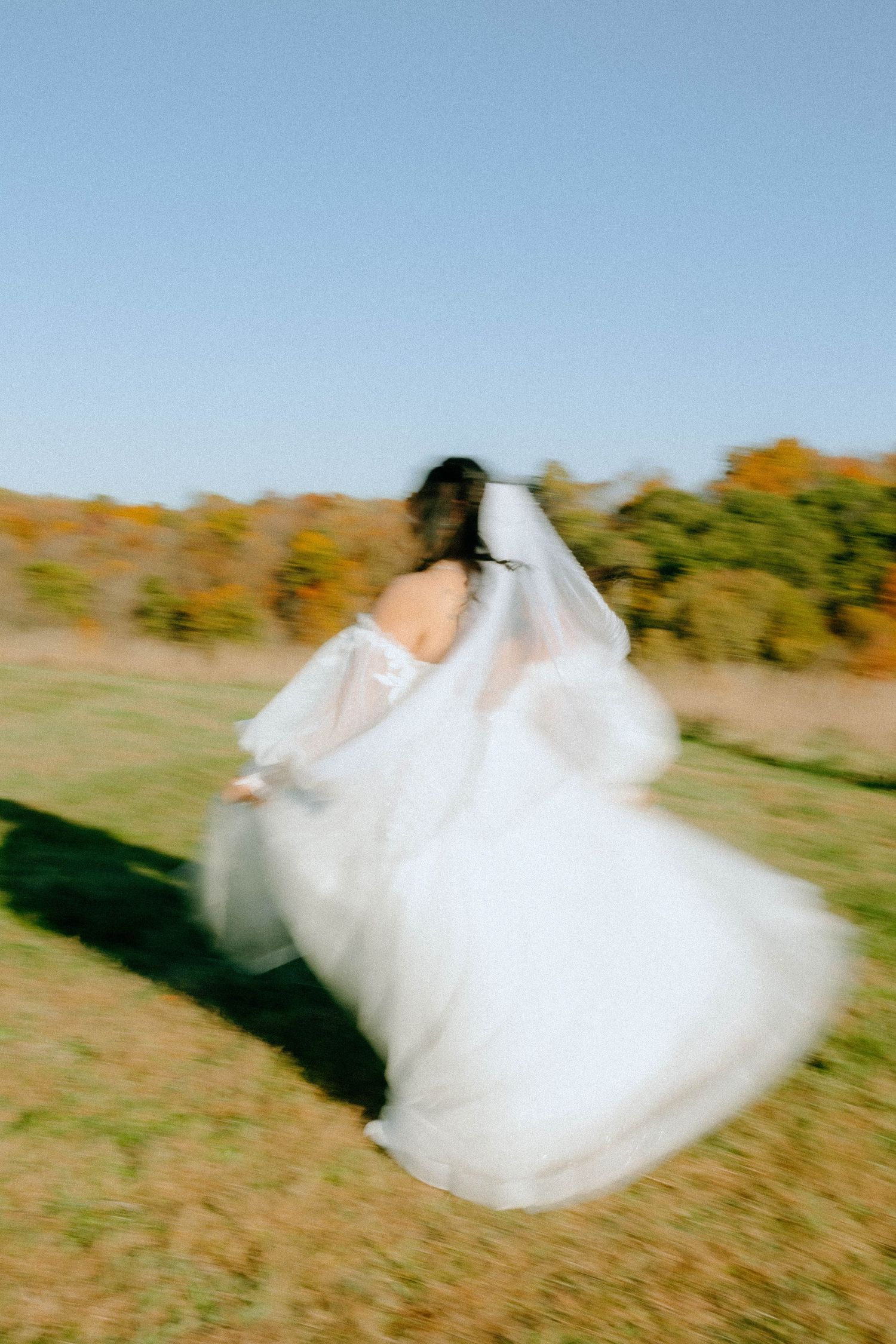 Motion-blur photograph of spinning white wedding dress in an autumn field.