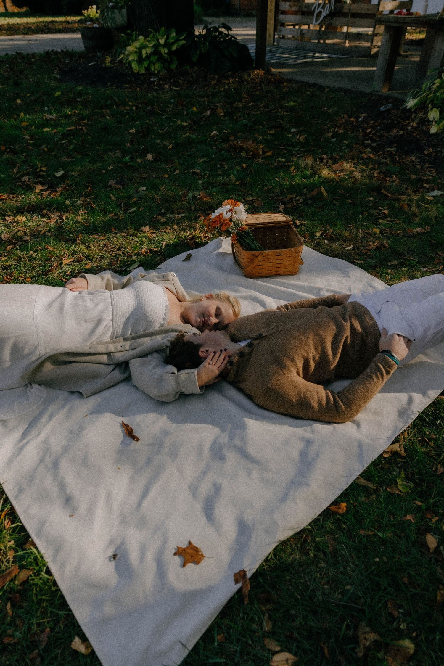 A couple relaxing on white blanket during autumn picnic with basket.