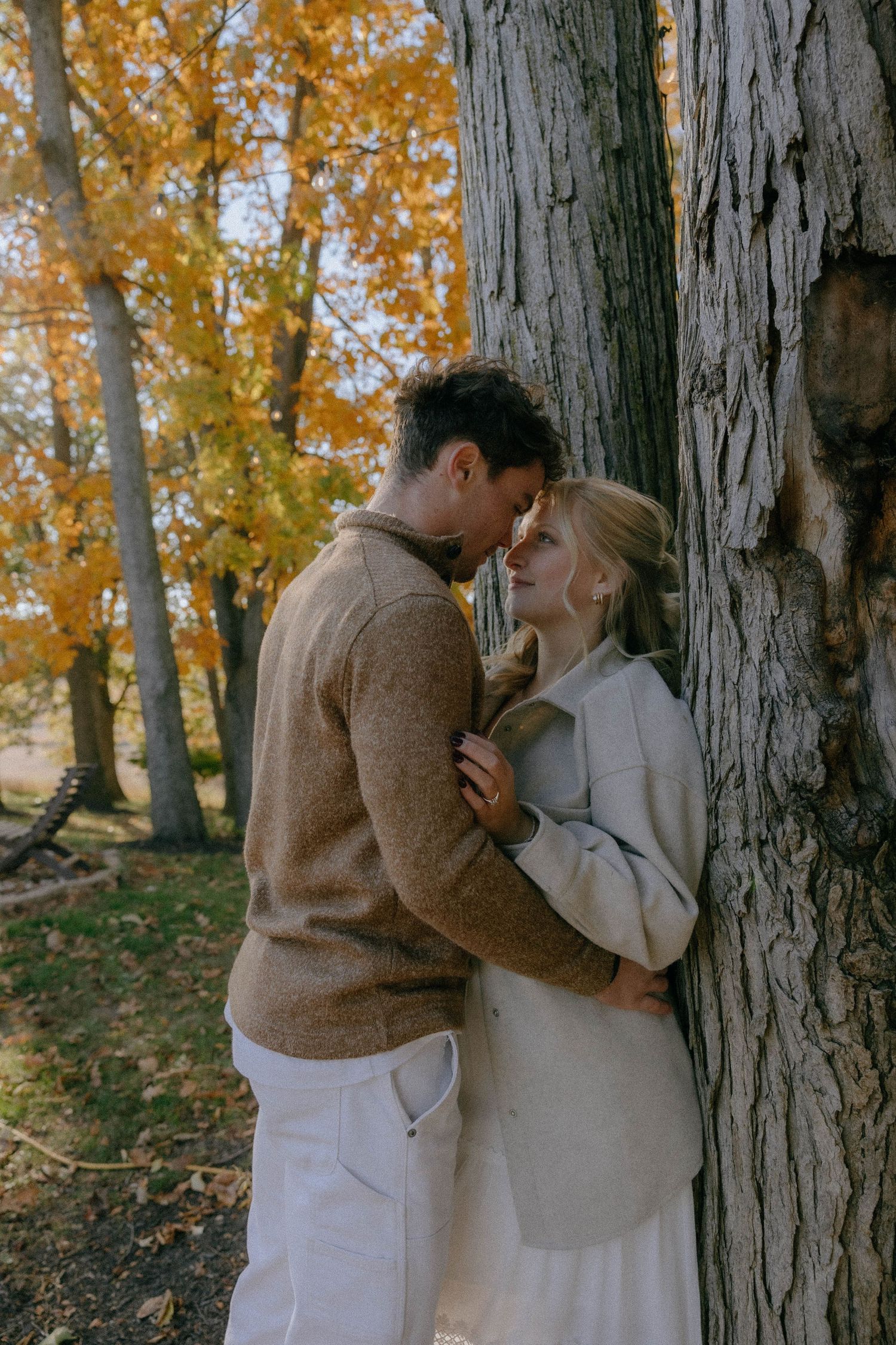 Romantic autumn moment between couple against tree trunk with fall foliage.