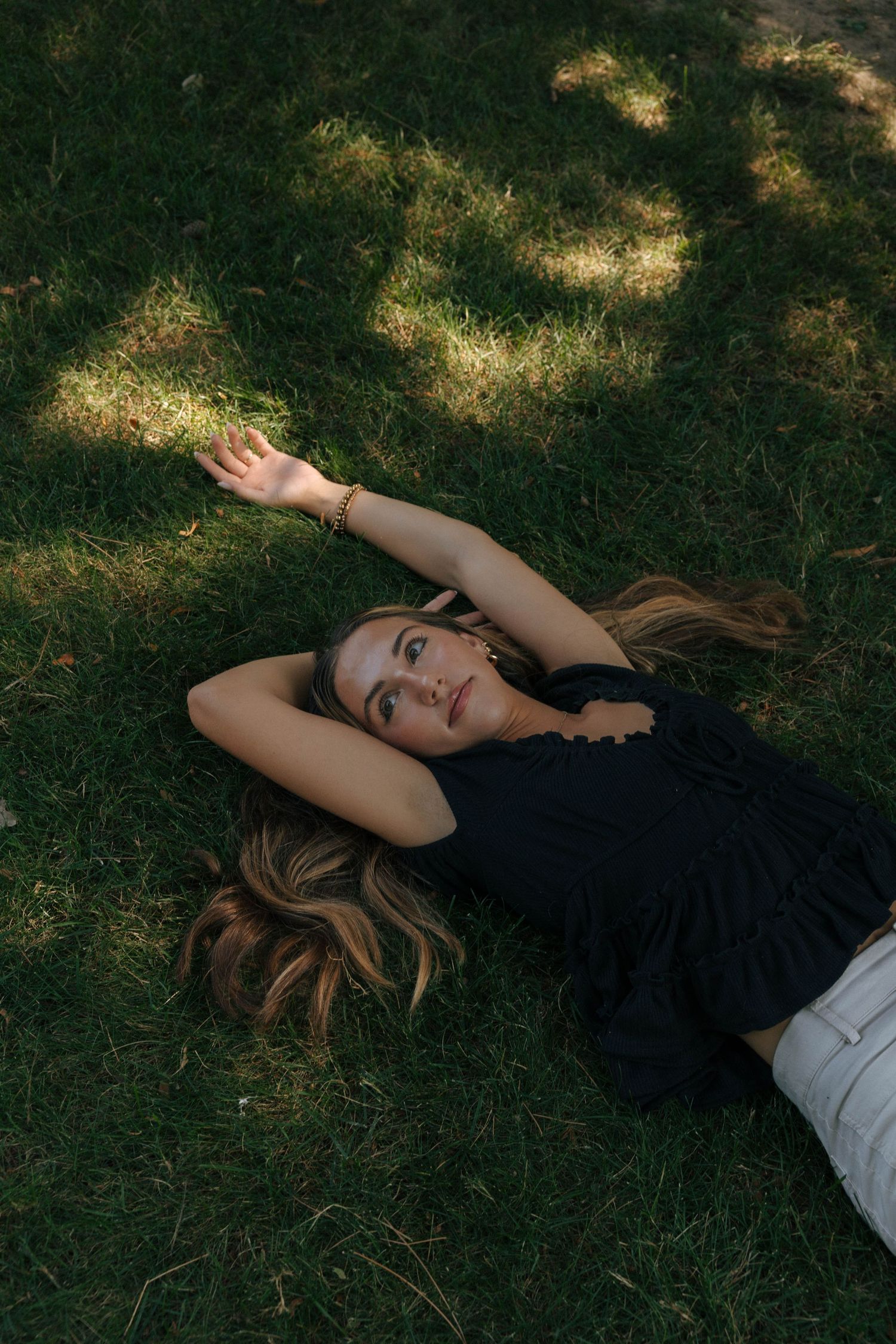 Artistic portrait lying on grass with dappled sunlight filtering through trees.