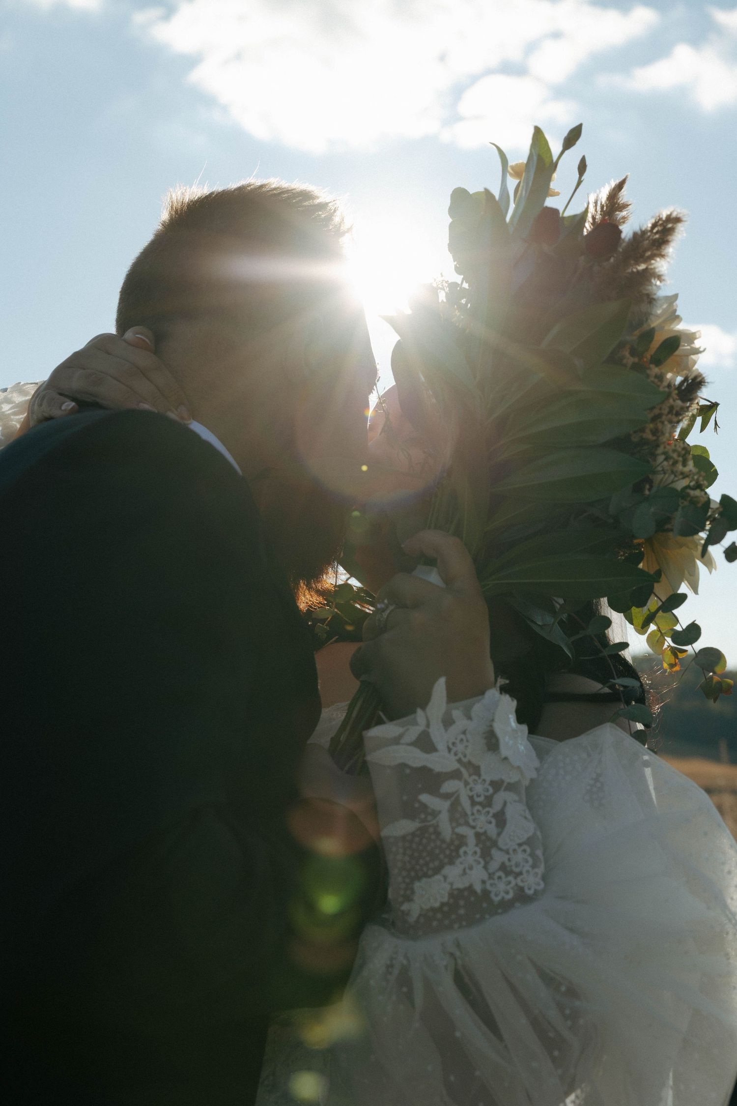 Backlit wedding couple silhouetted against bright sunlight and autumn foliage.