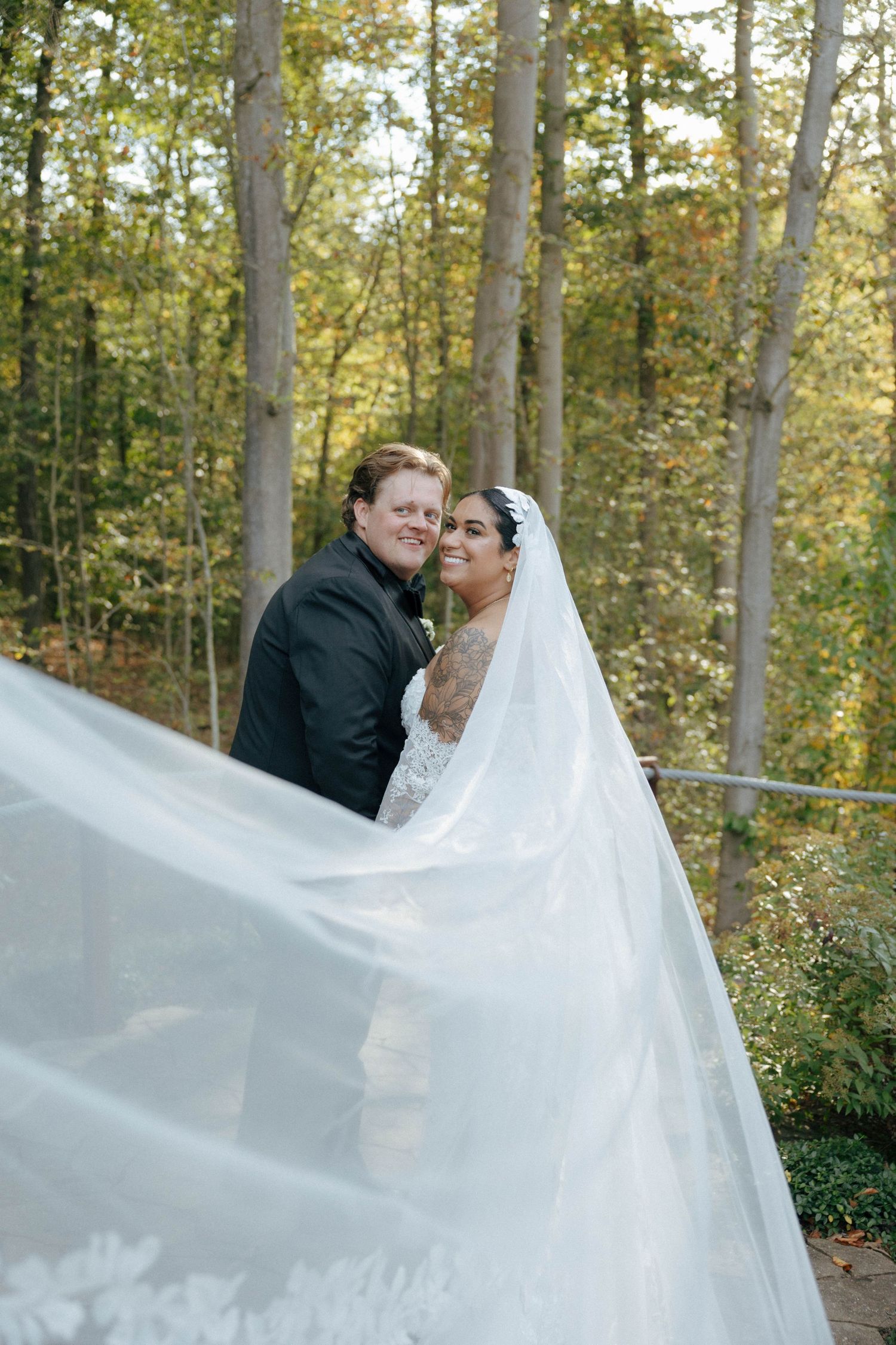 Wedding portrait with flowing white veil against autumn forest backdrop.