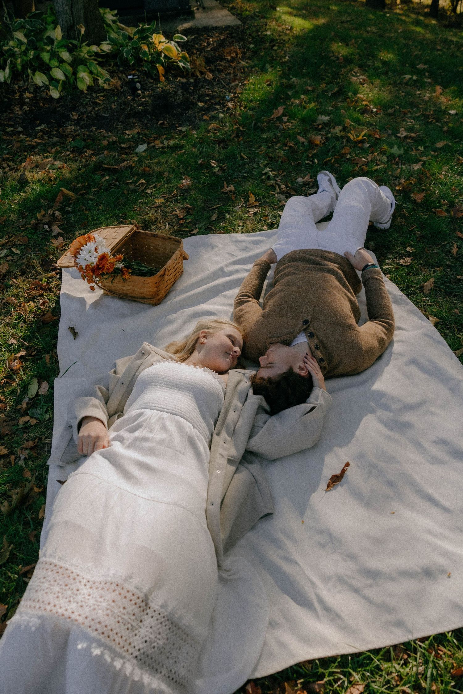 Two people rest peacefully on a white blanket in a wooded autumn setting.