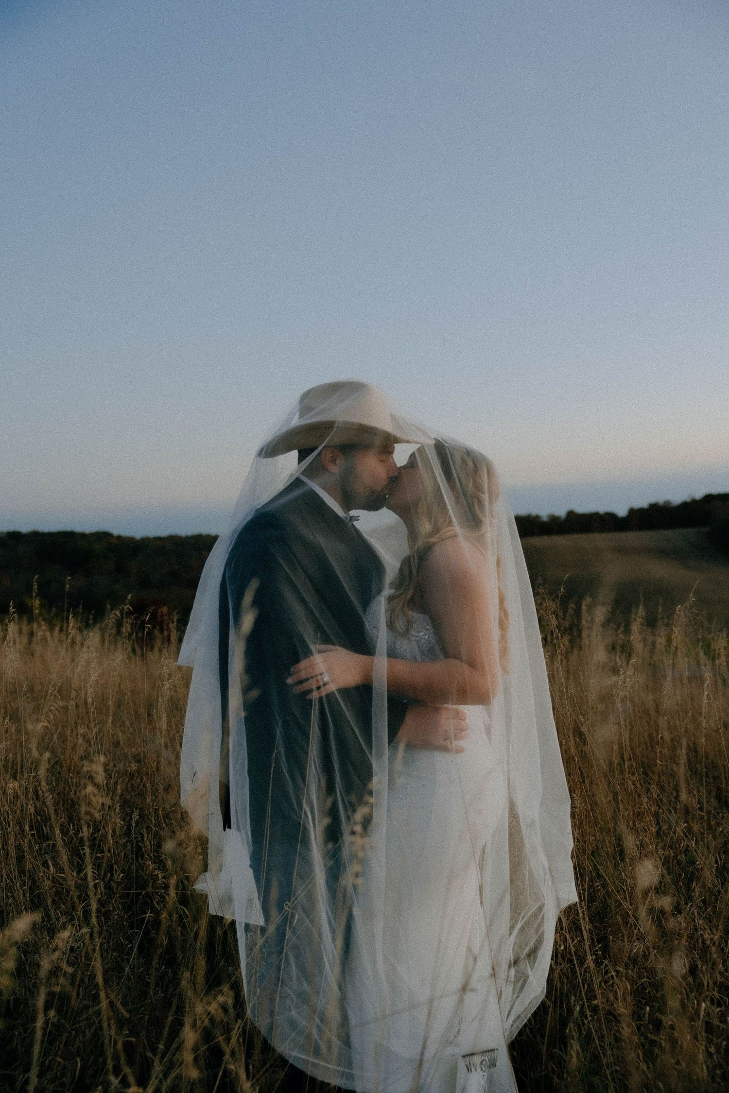 Ethereal wedding couple embracing in a misty field at dusk.