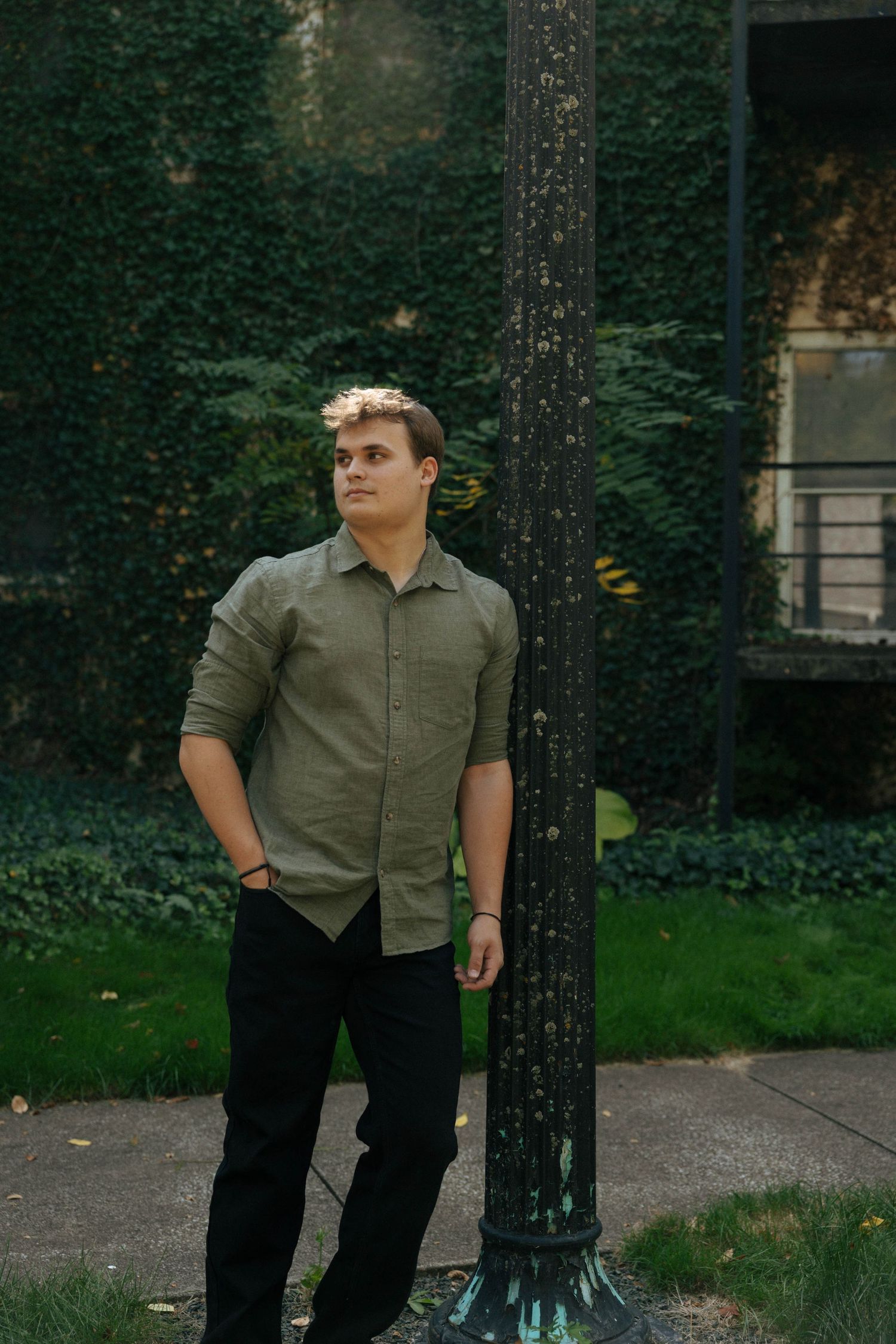 A casual portrait of a person in an olive shirt standing against an ivy-covered wall.