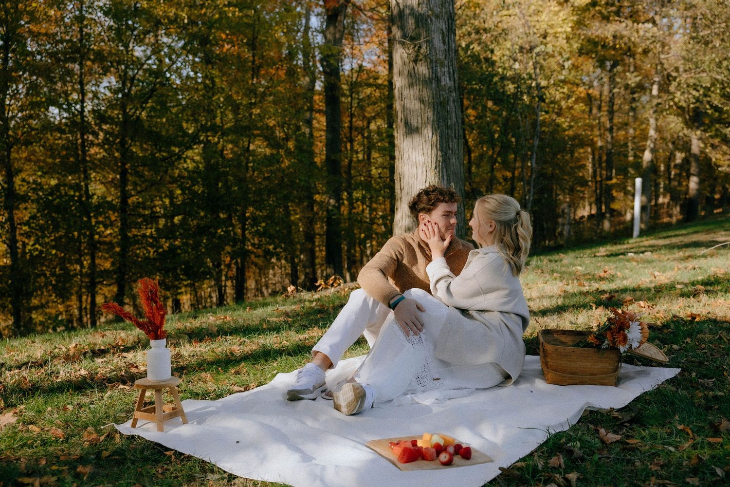 A couple enjoying a romantic autumn picnic on a white blanket surrounded by fall foliage.