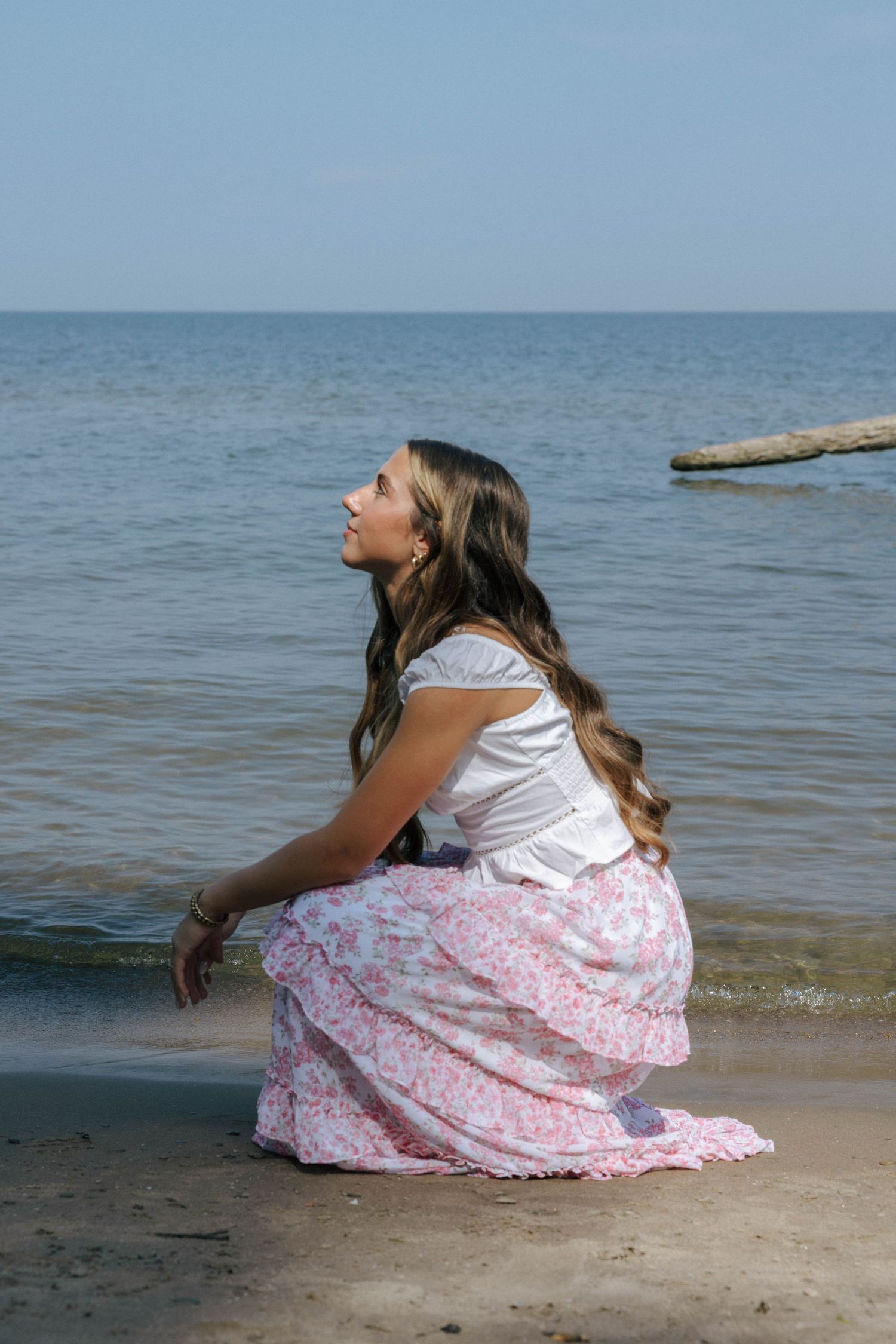 A woman in a floral skirt sits by the waterfront on a sunny day.