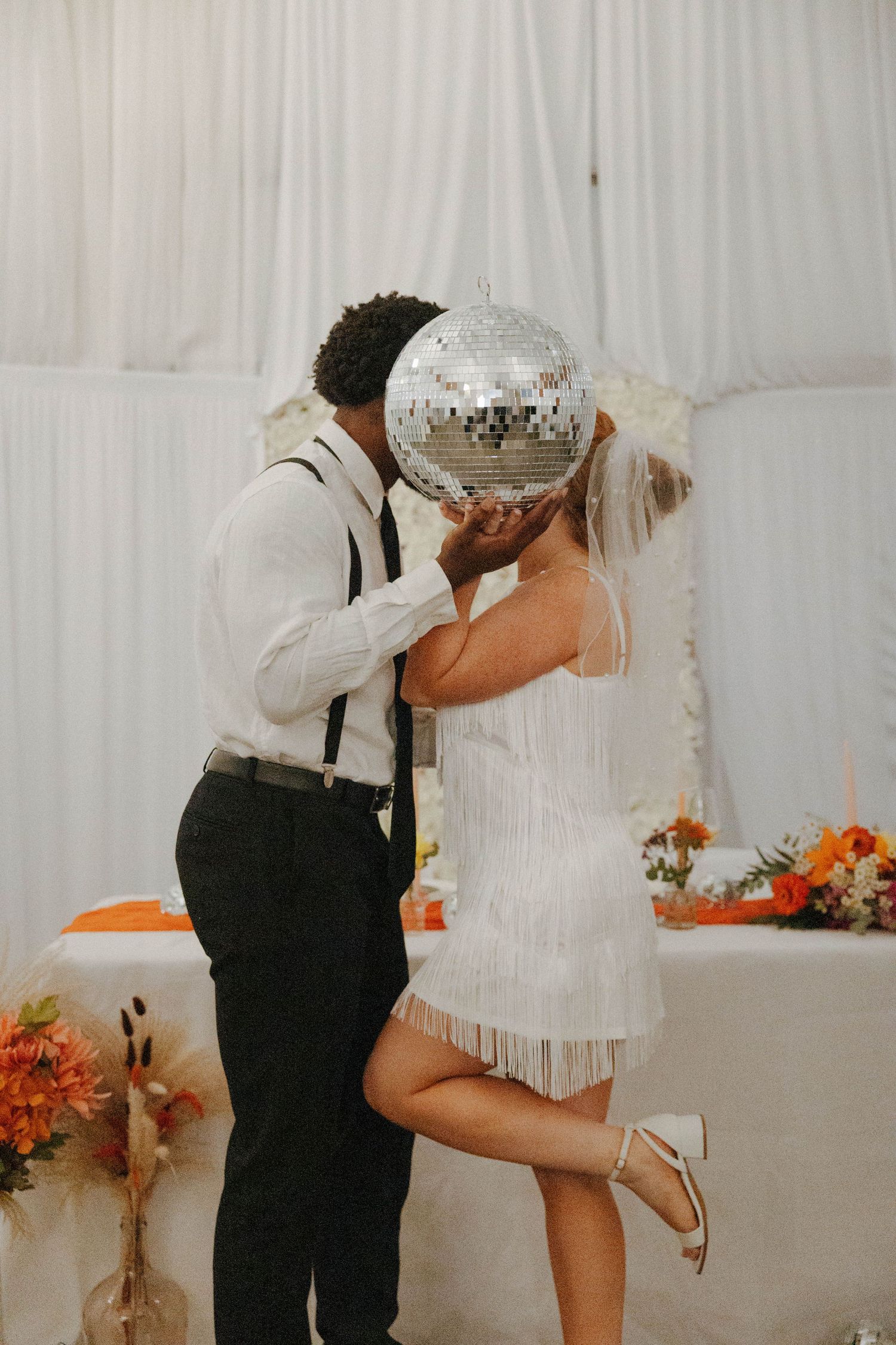 Couple sharing romantic moment behind disco ball in vintage-inspired wedding reception.