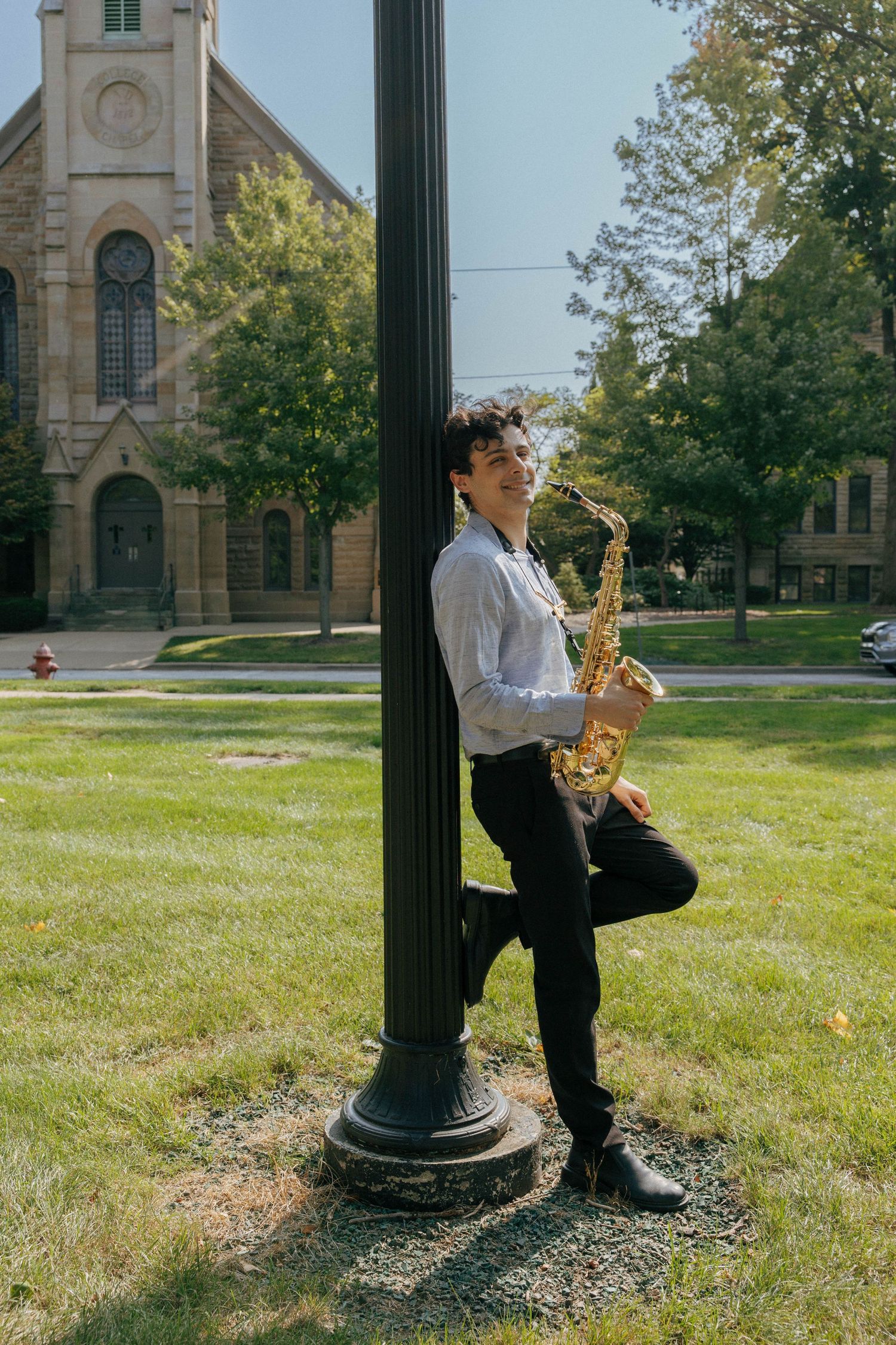 Saxophone player performing near a lamp post with historic church buildings in background.