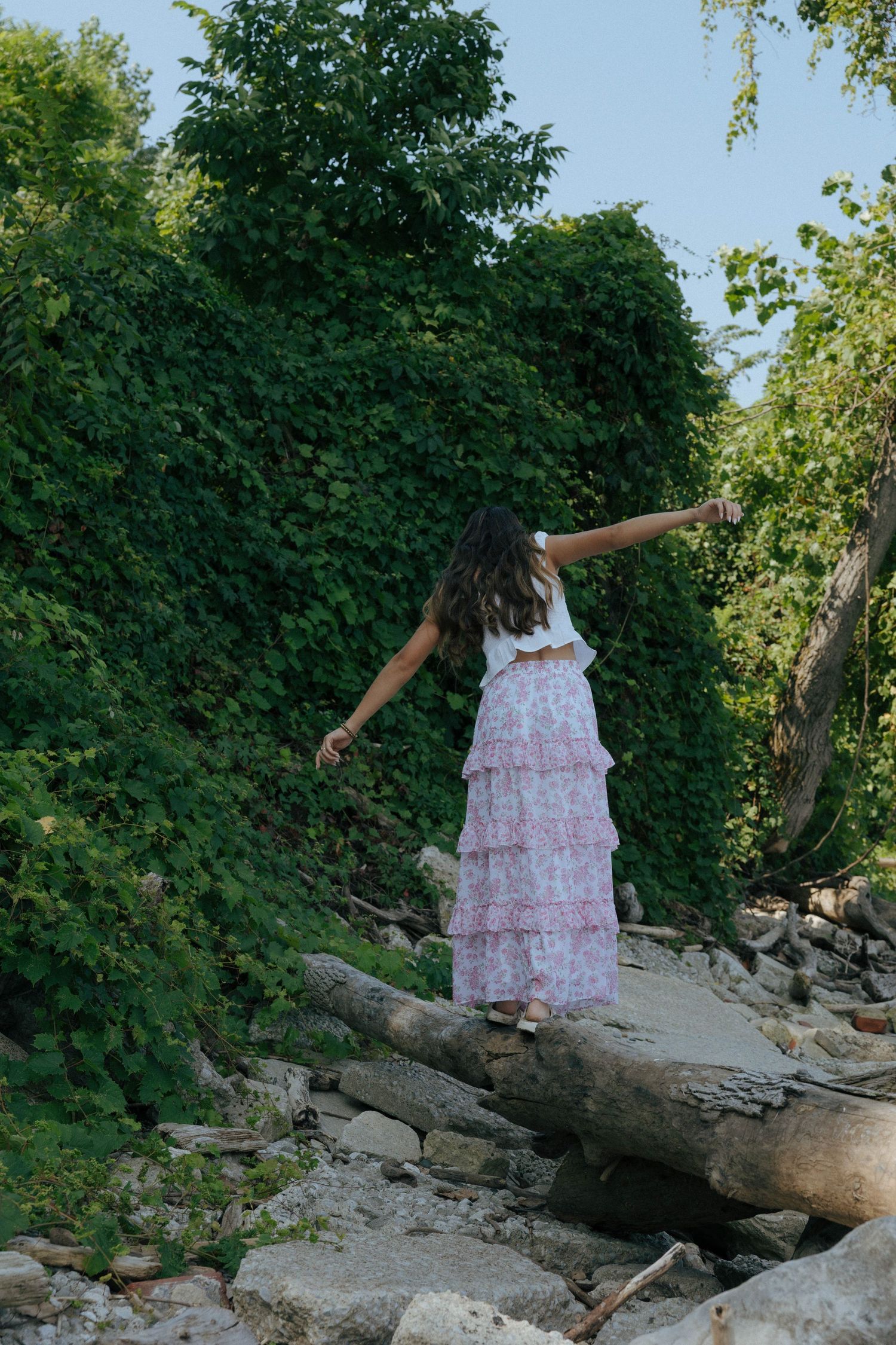 A playful sequence of someone balancing on a fallen log in a pink dress against green foliage.