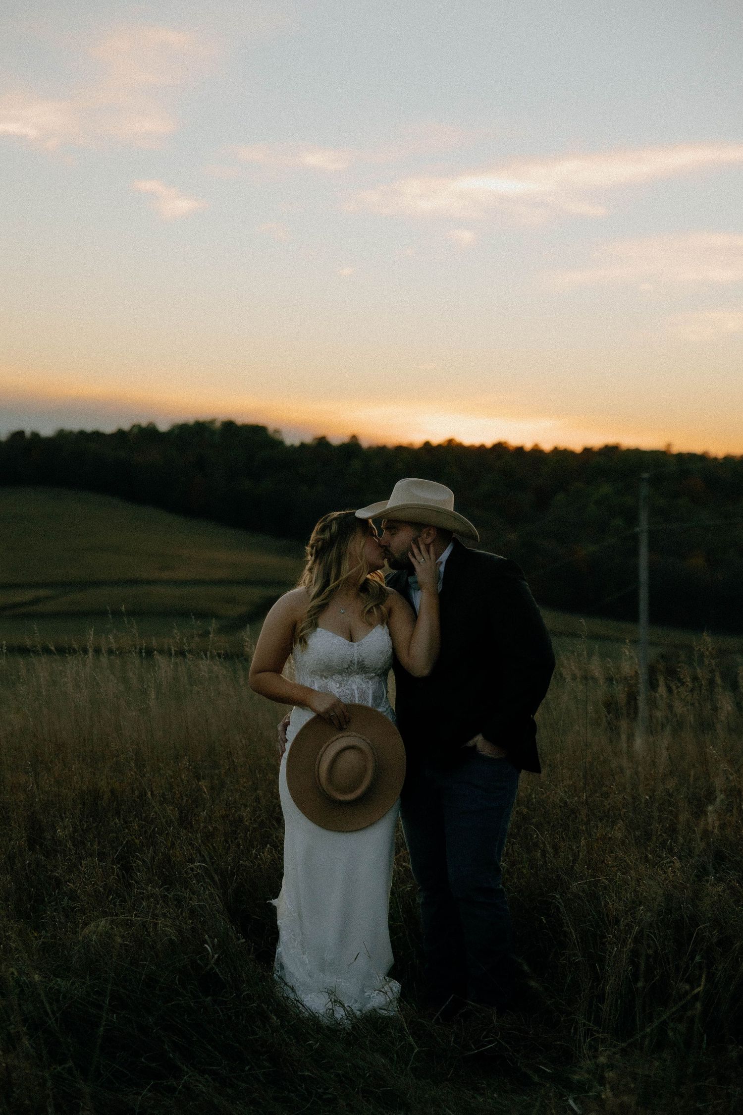 A couple wearing cowboy hats poses playfully in a golden field at sunset.