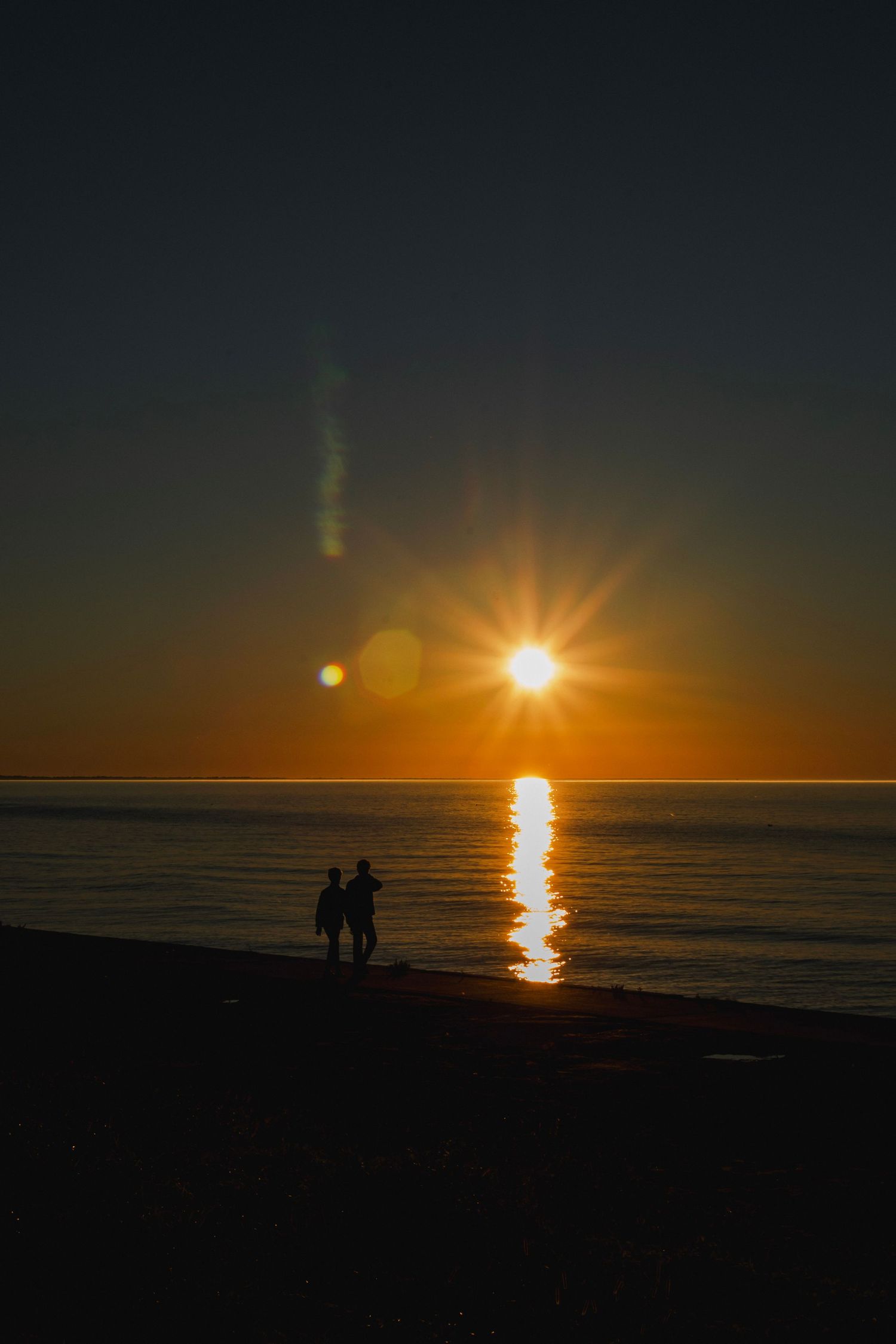 Moody couple silhouette at sunset over Lake Ontario, Webster NY pier. High-contrast Velvet Hour session portrait.