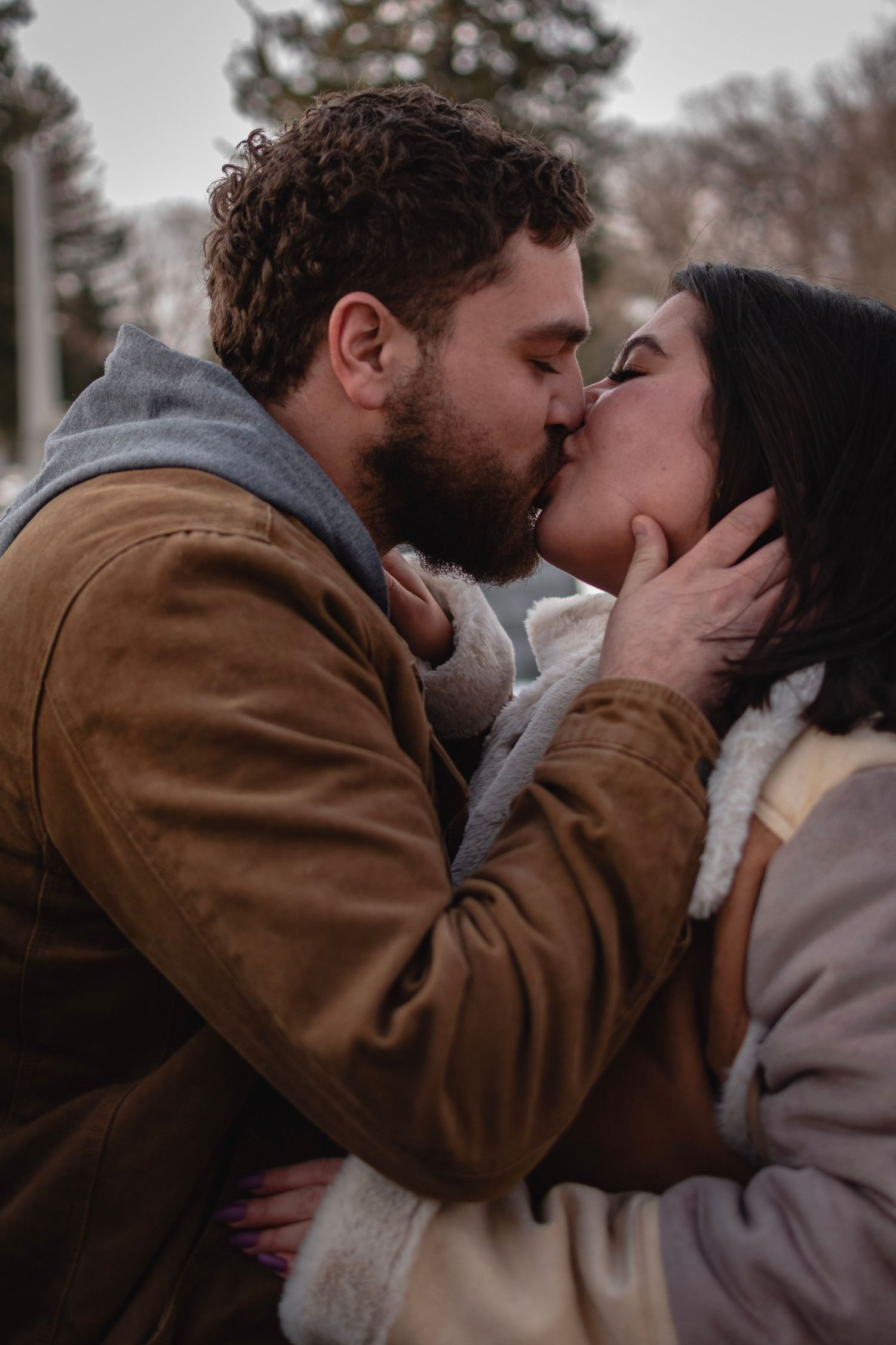 Intimate close-up color photo of couple kissing in winter at Mt. Hope Cemetery, Rochester NY. Dramatic portrait.