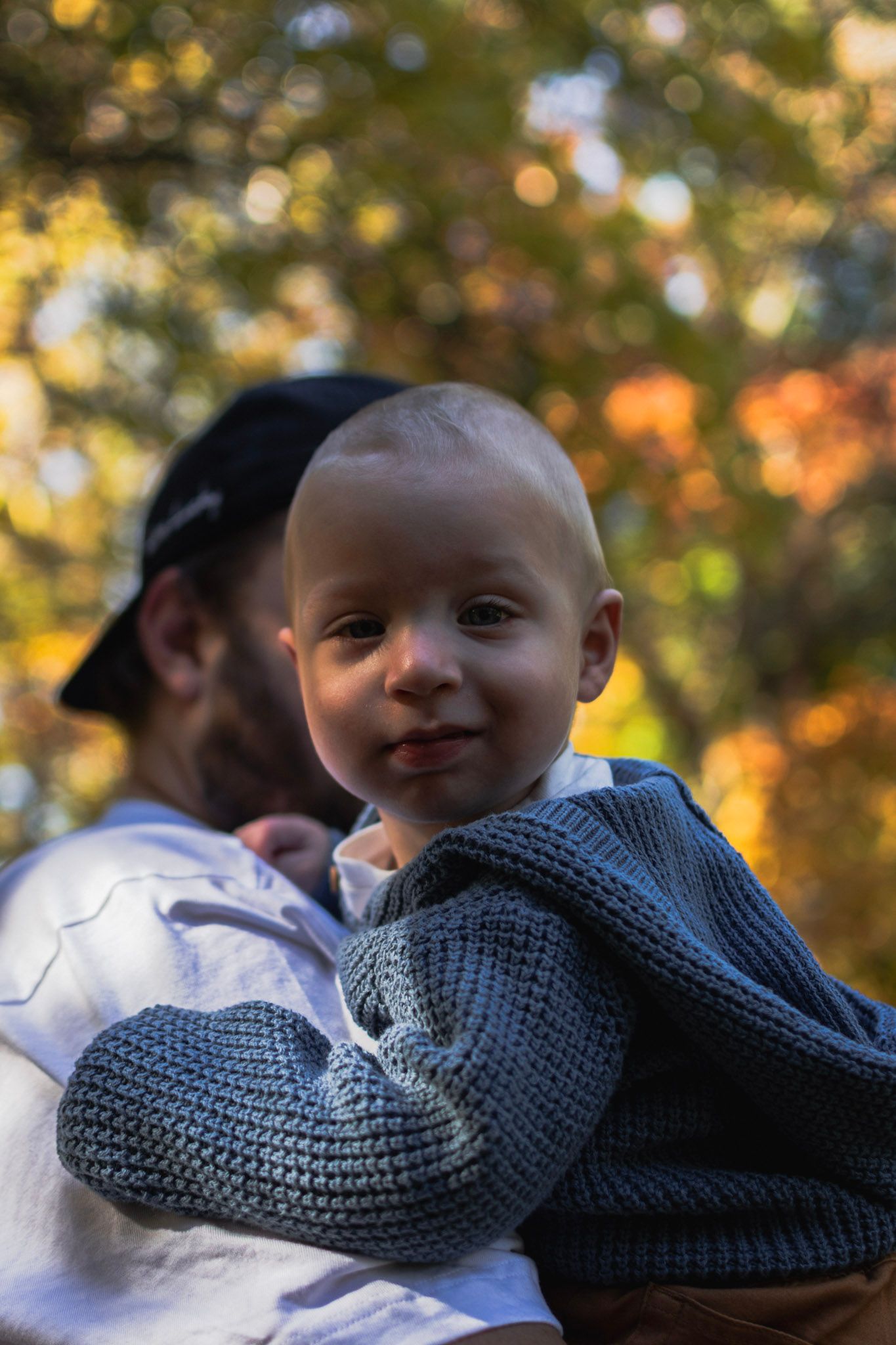 Candid toddler portrait at Zoo Road in Rochester, NY, featuring a blue knit sweater and warm autumn bokeh.