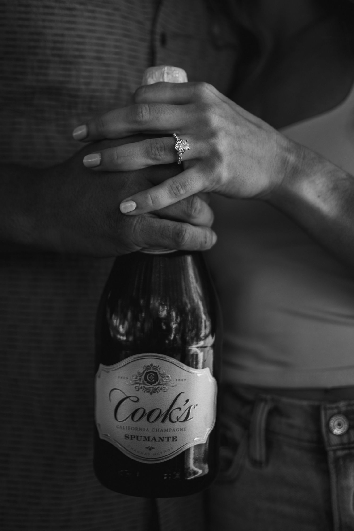 B&W close-up of couple celebrating with champagne and ring at Webster Park, NY. Candid summer portrait.