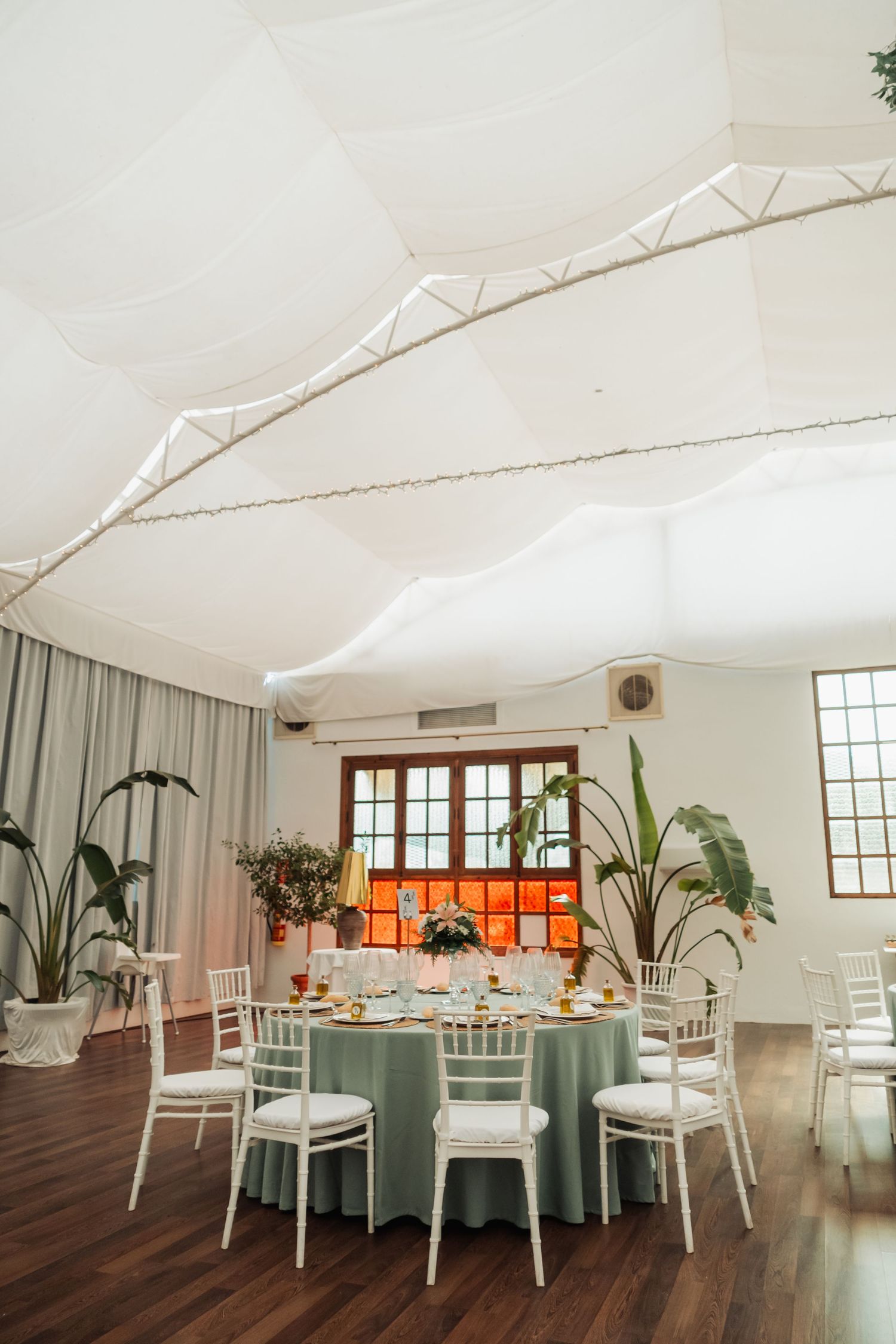 Elegant wedding reception hall with sage green tablecloths, white Chiavari chairs, and draped ceiling.