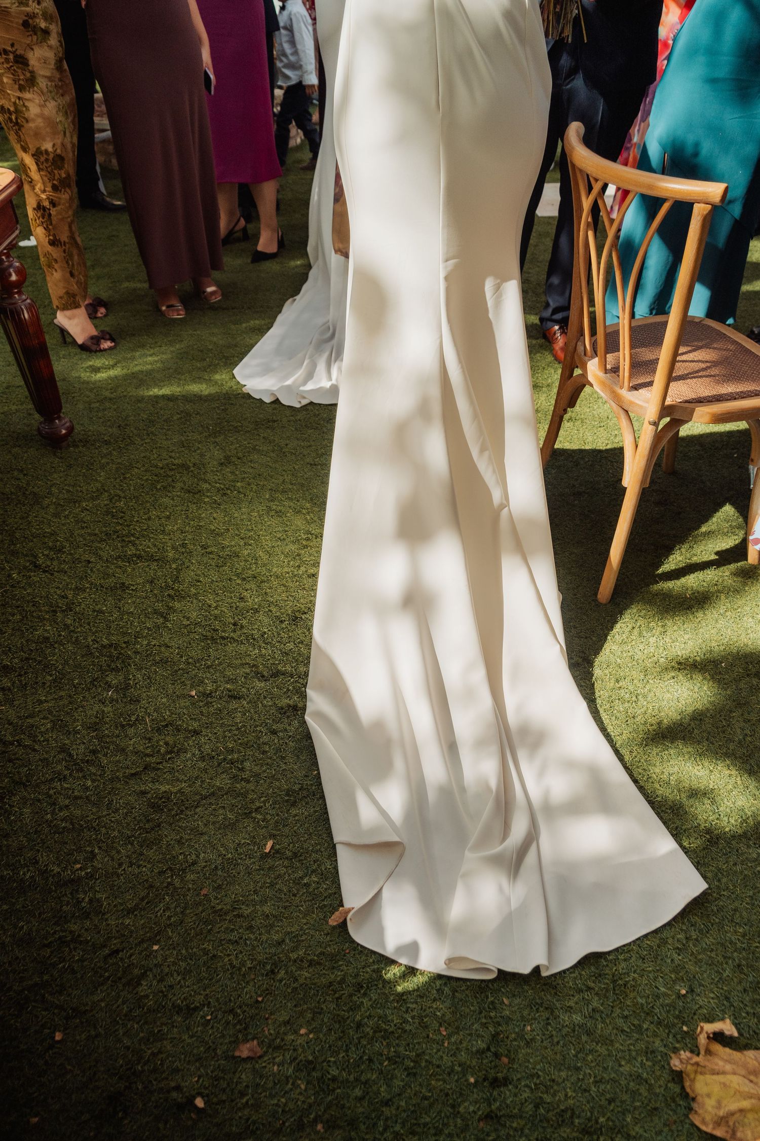 Close-up of a bride's elegant white satin wedding gown train on green grass at an outdoor ceremony.