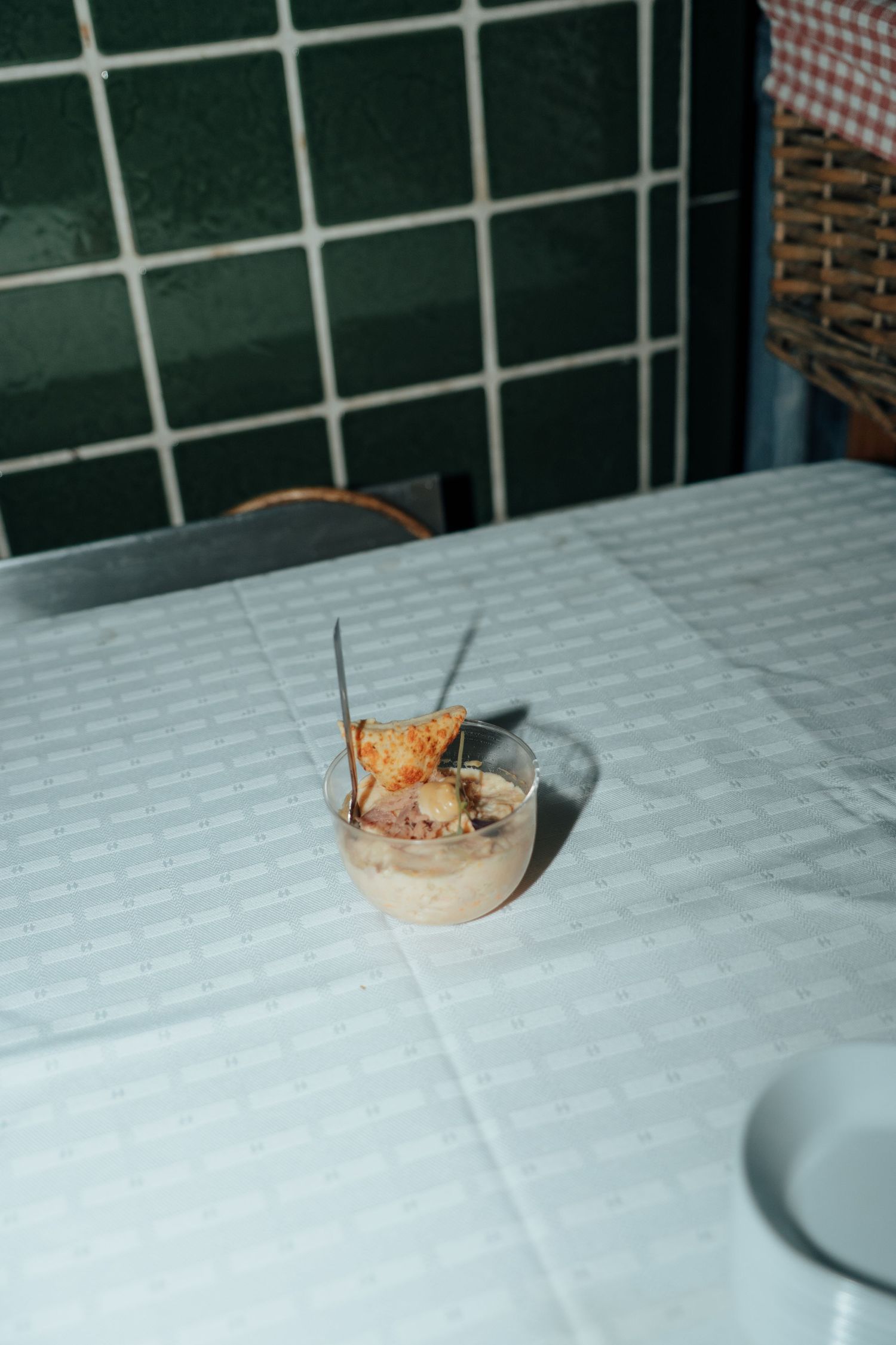 Small glass dessert cup with toast garnish served on a white tablecloth near green tiles.
