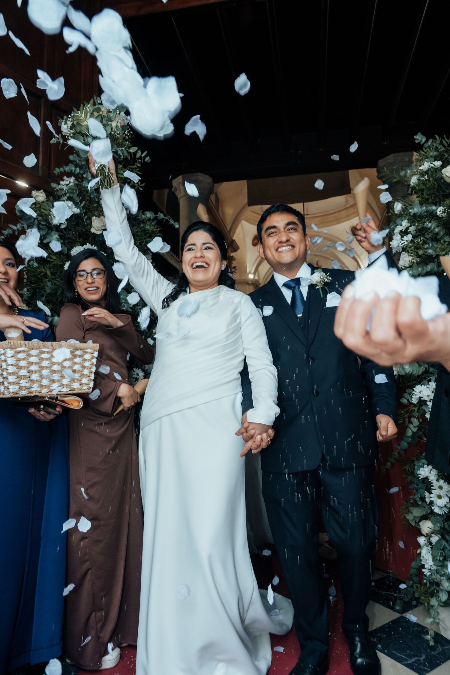 Joyful bride and groom exit church as guests toss white flower petals in celebration.