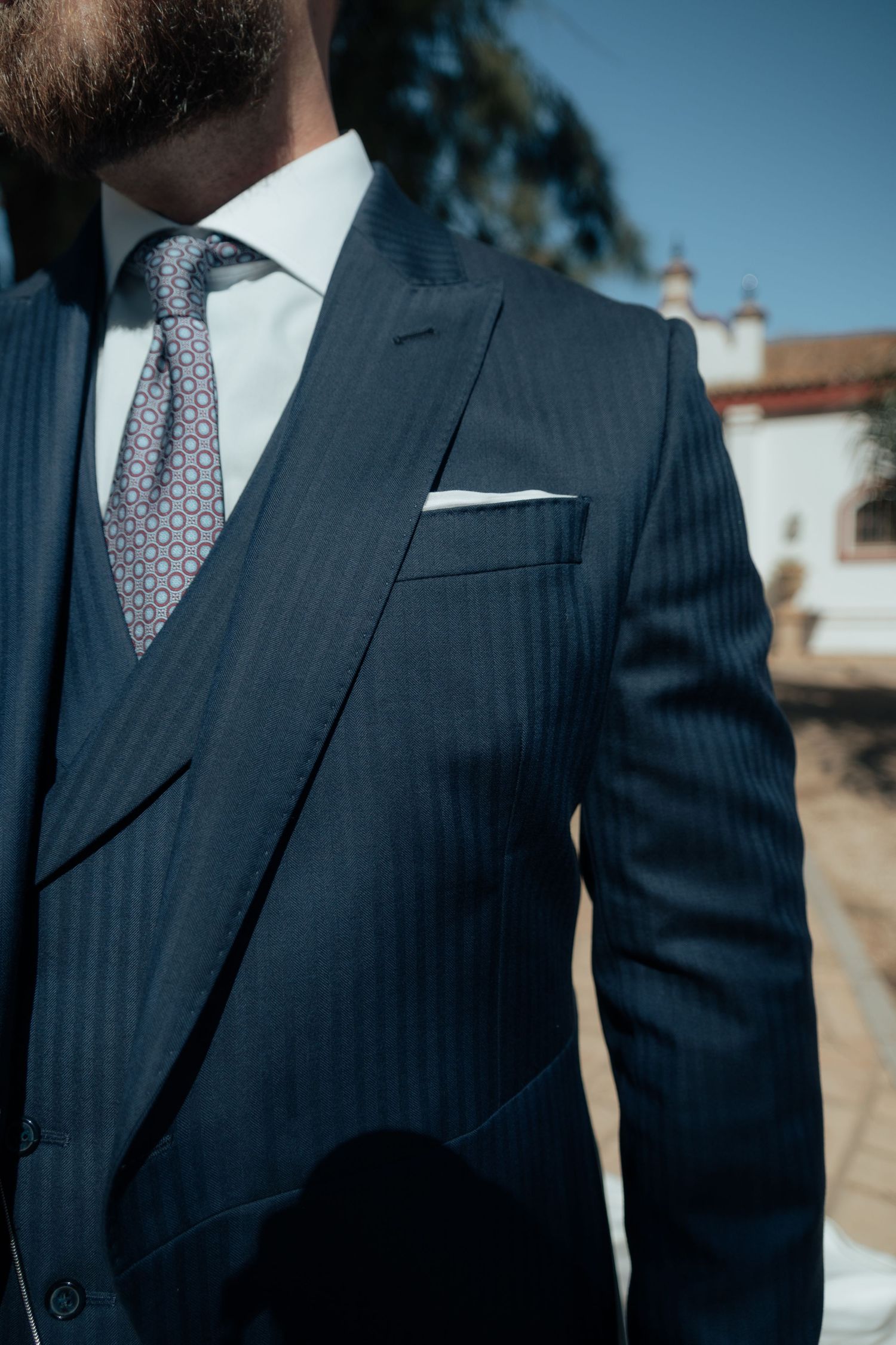 Close-up of groom's elegant navy pinstripe three-piece suit with patterned tie and white pocket square.
