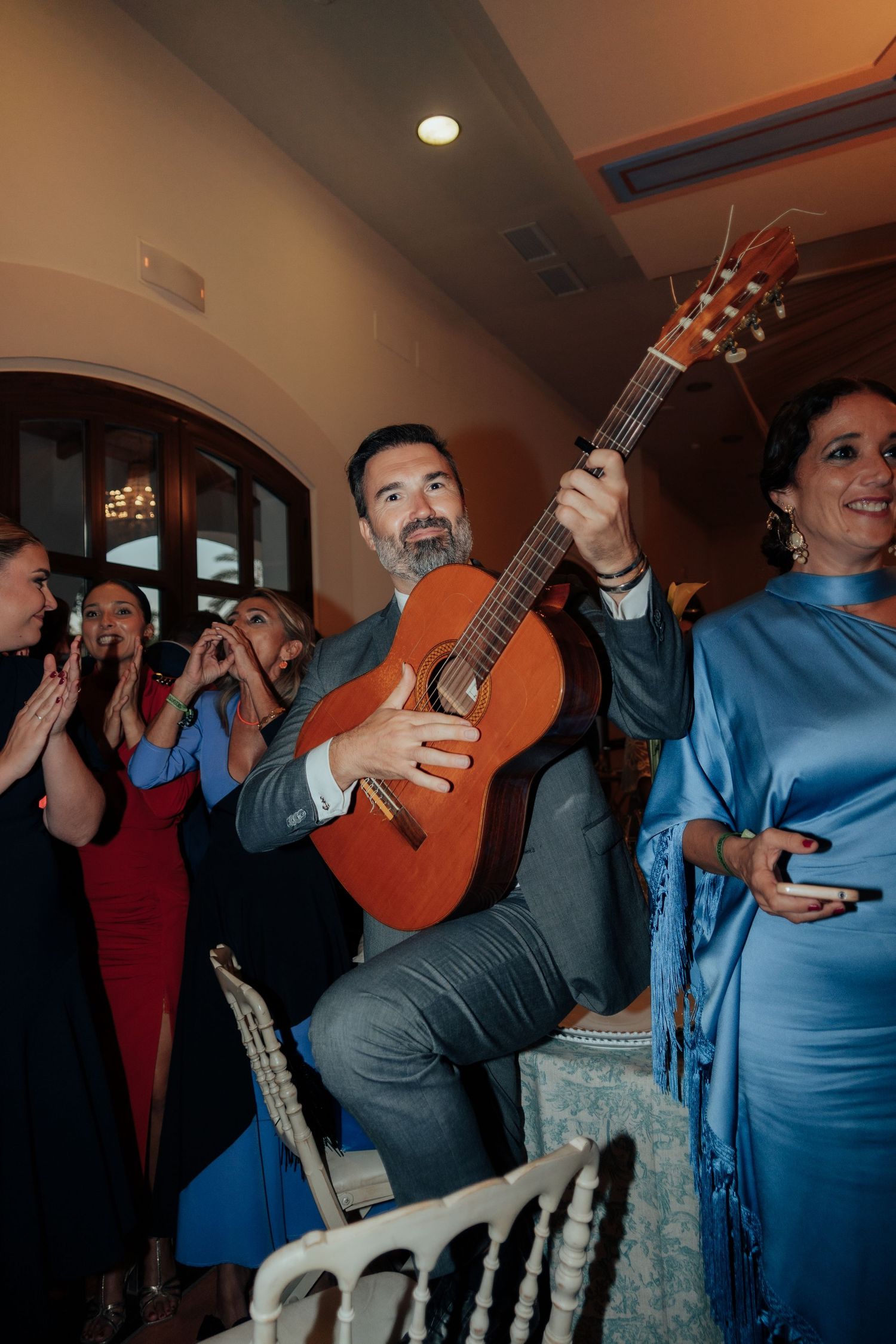 Wedding guest playing acoustic guitar while woman in blue dress stands beside him at reception.