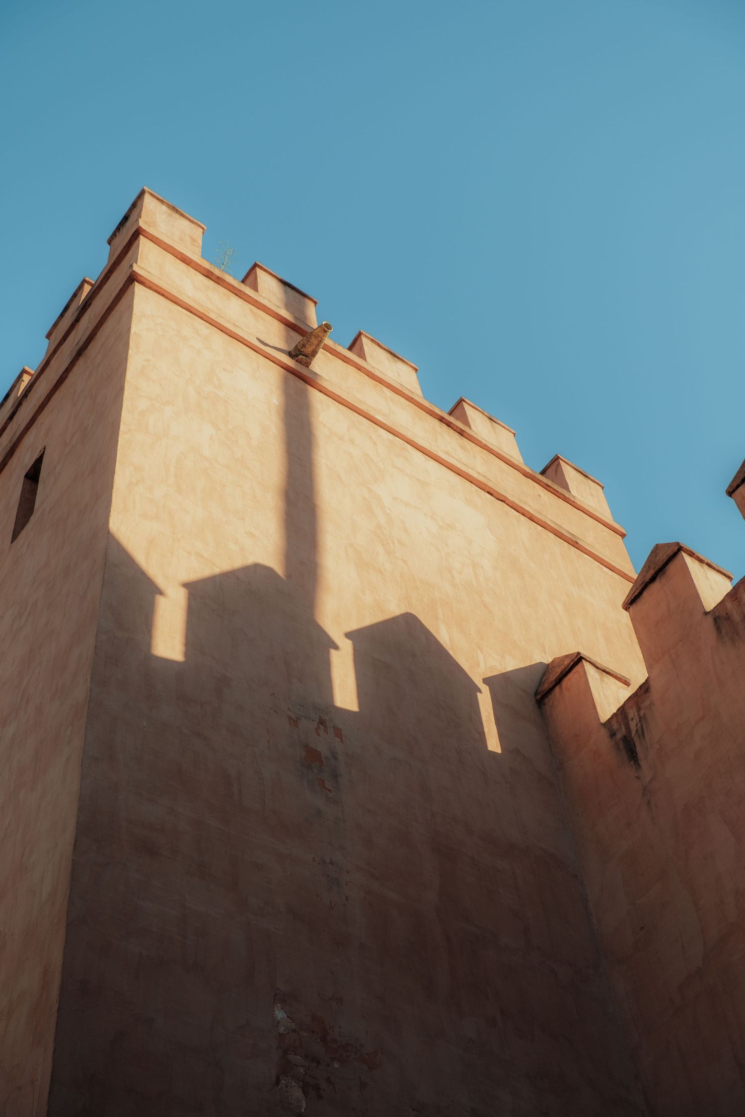 Low angle view of a sunlit ancient stone tower with battlements against a clear blue sky in Seville.