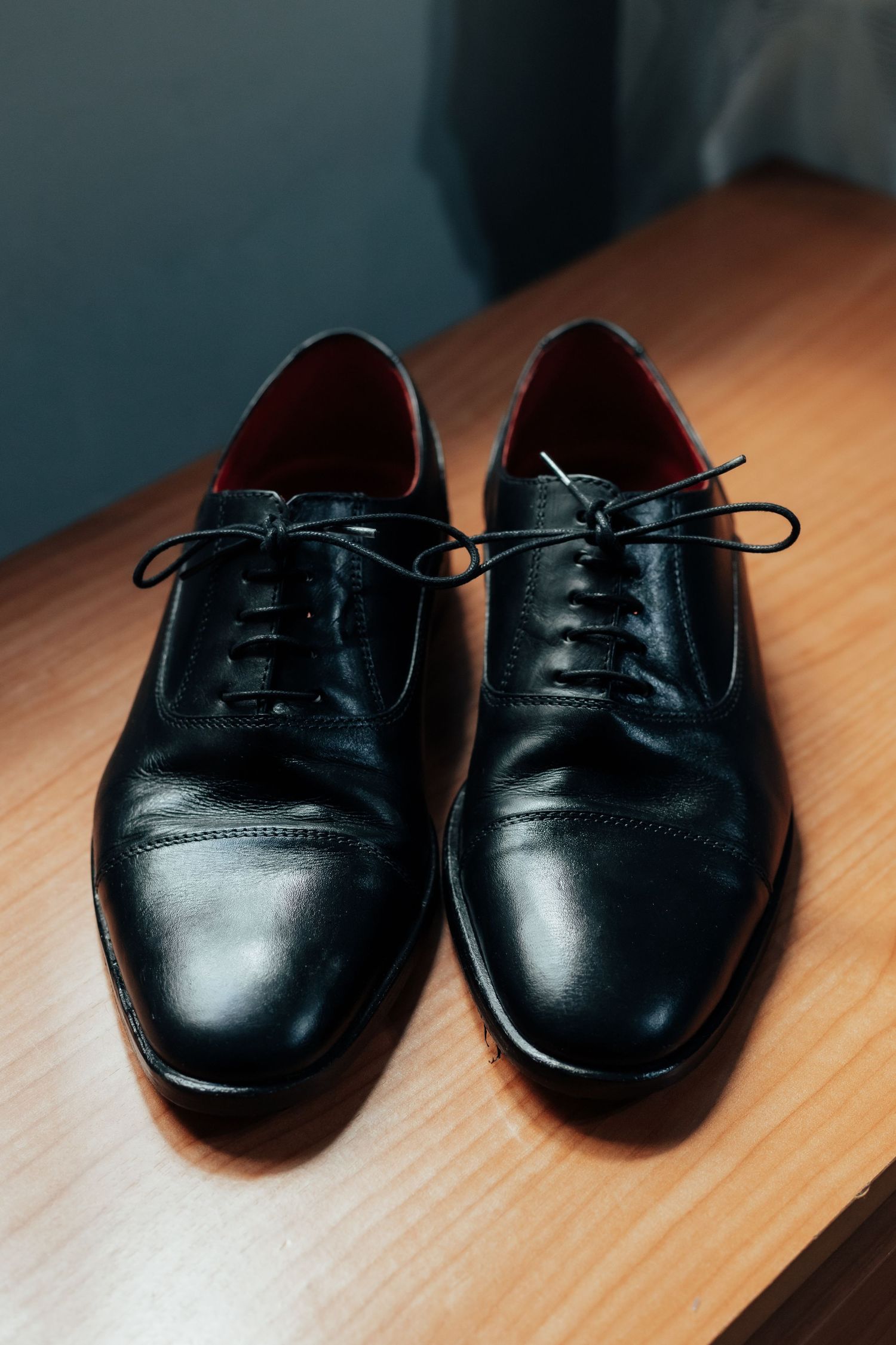 Pair of polished black leather Oxford dress shoes placed on wooden surface.