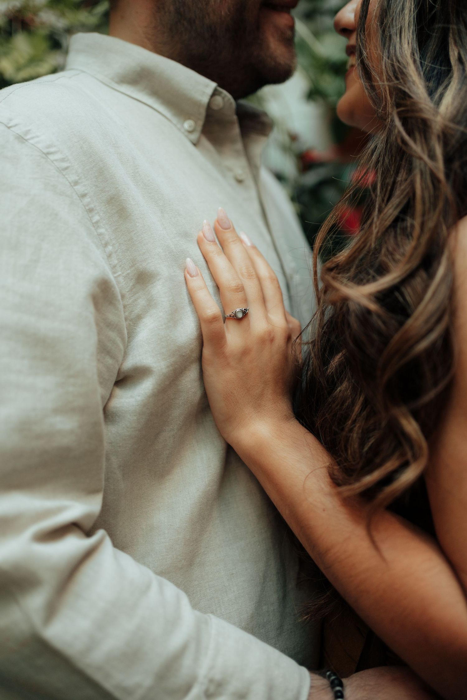 Close-up of a woman's hand with an engagement ring resting on a man's chest during a romantic couple's photo shoot.