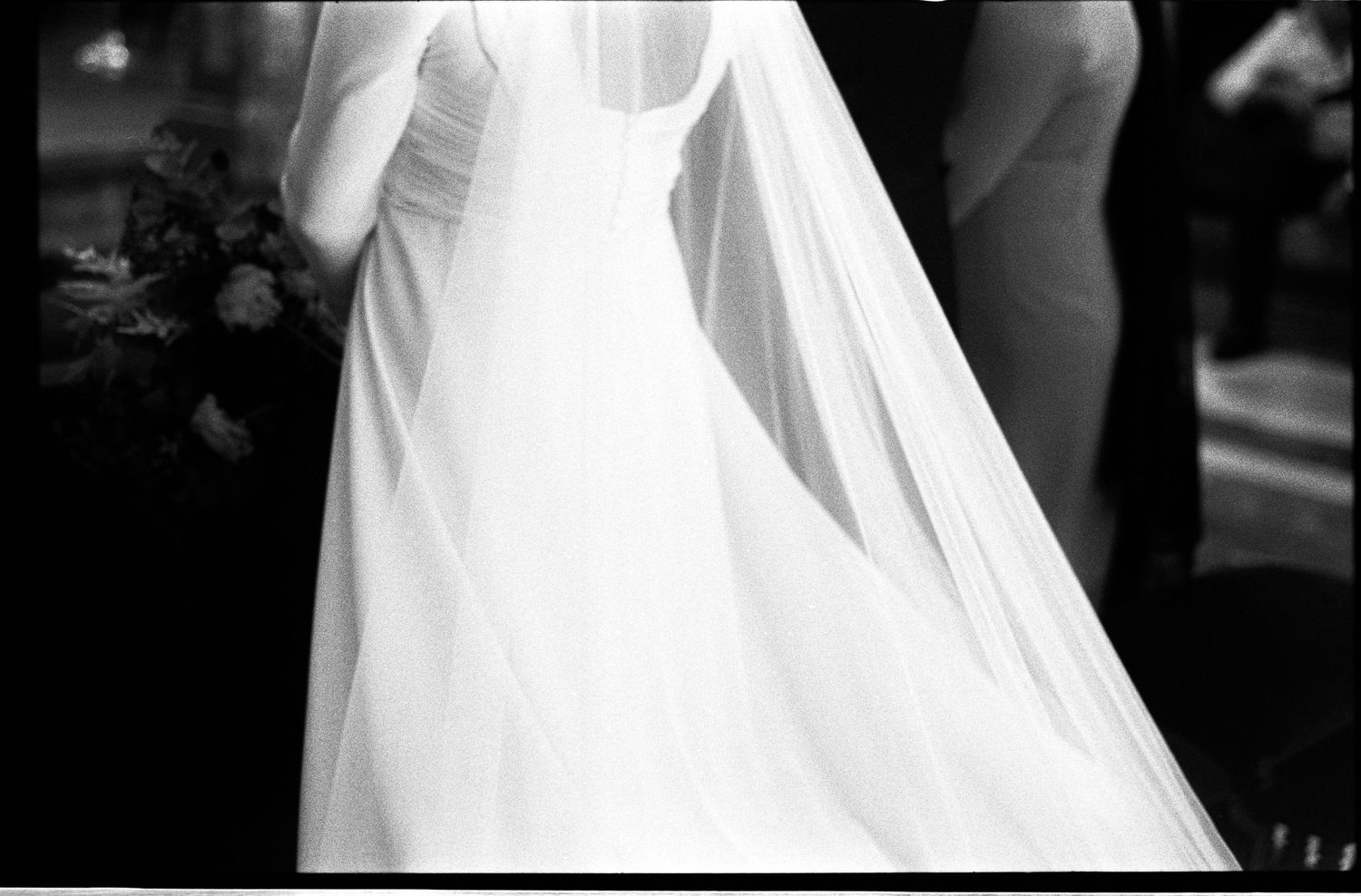 Elegant black and white photo of bride in long white gown and veil holding bouquet at church wedding.