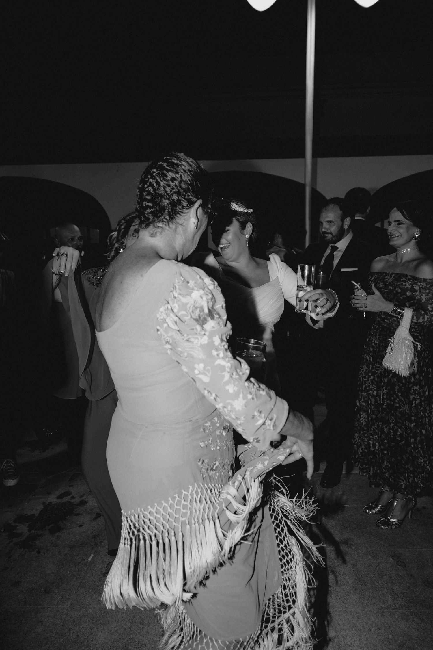 Black and white photo of guests dancing at a lively evening wedding reception.
