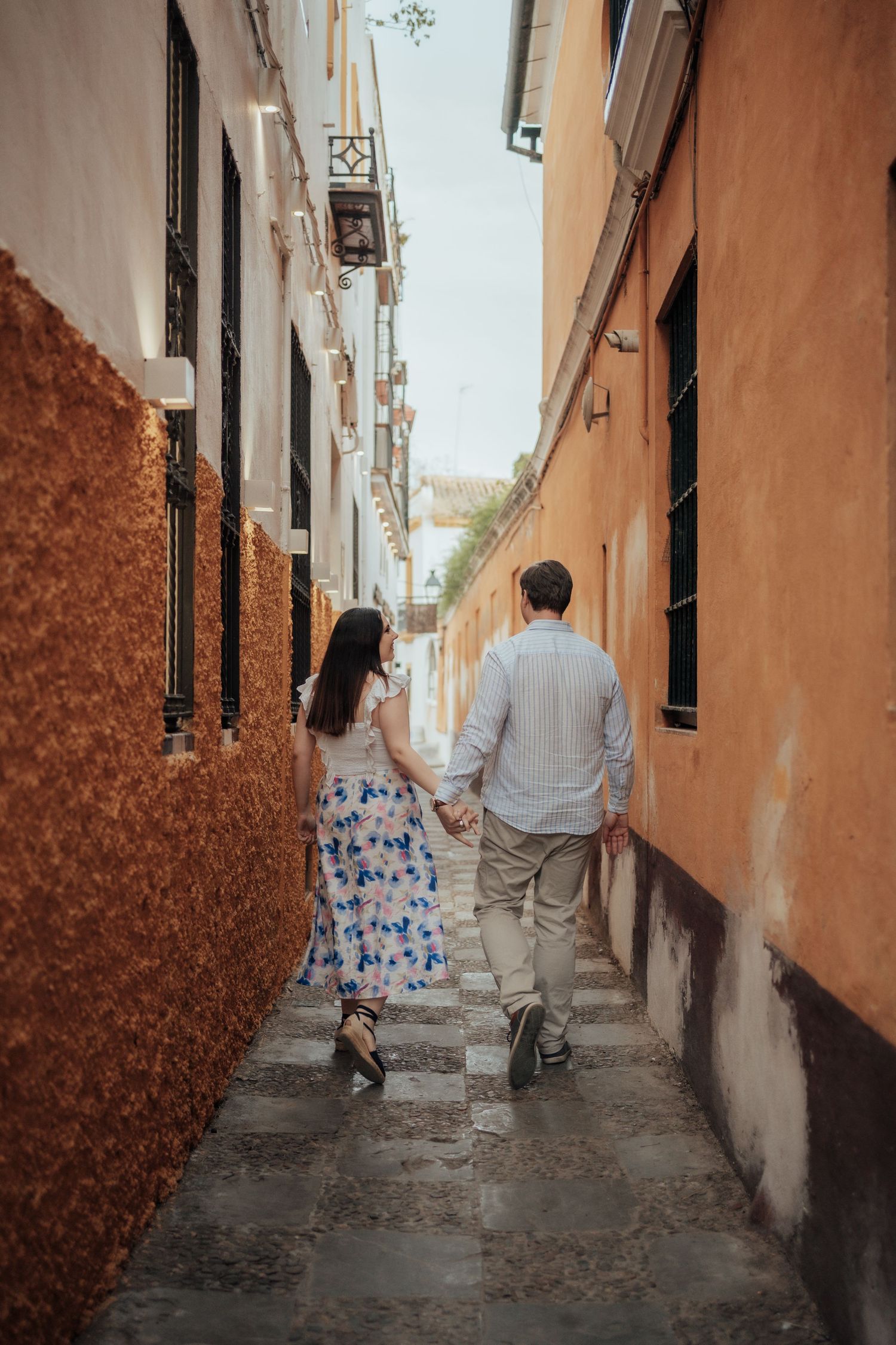 Couple holding hands walking through a narrow cobblestone alley with colorful walls.
