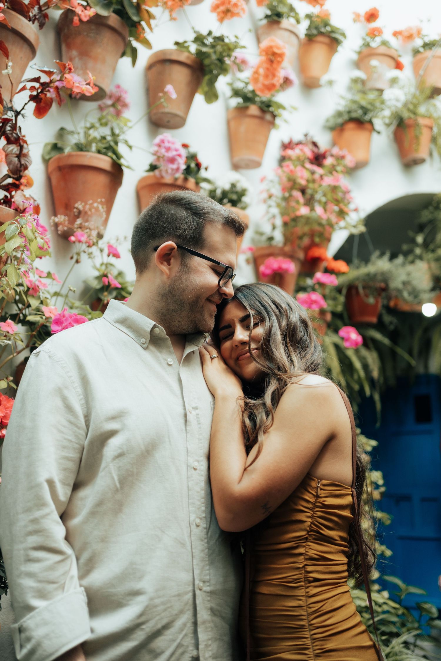 Couple sharing a tender moment in front of a colorful wall of terracotta flower pots in bloom.