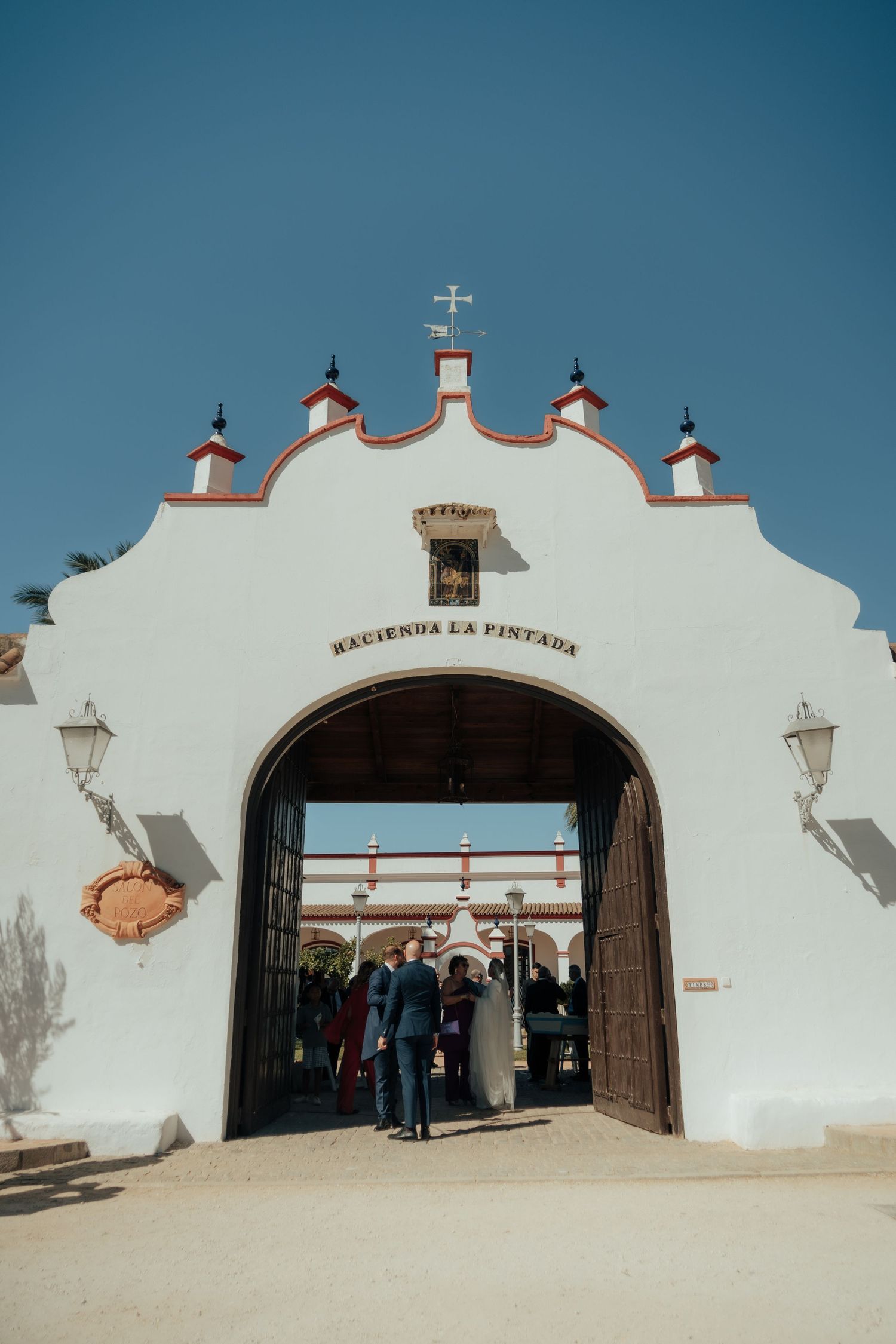 Bride and groom stand at the grand arched entrance of Hacienda La Pintada on their wedding day.