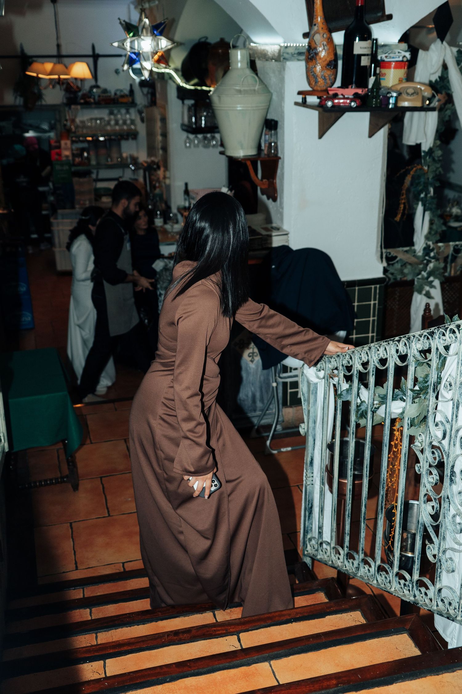 Woman in long brown dress descending stairs inside a rustic restaurant during a social event.
