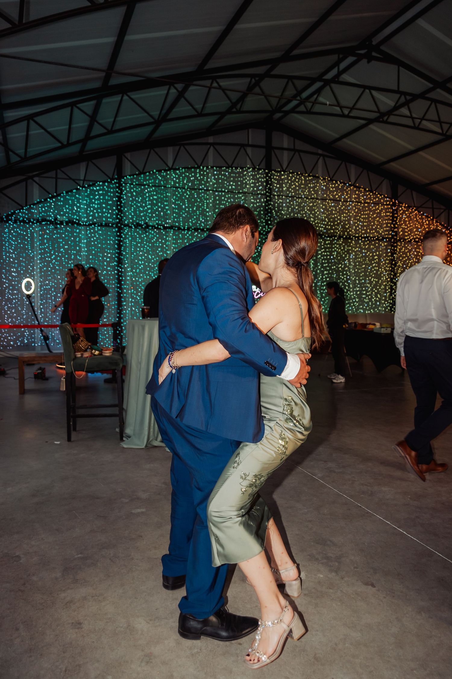 Couple sharing a romantic kiss on the dance floor at an elegant wedding reception with twinkling lights.