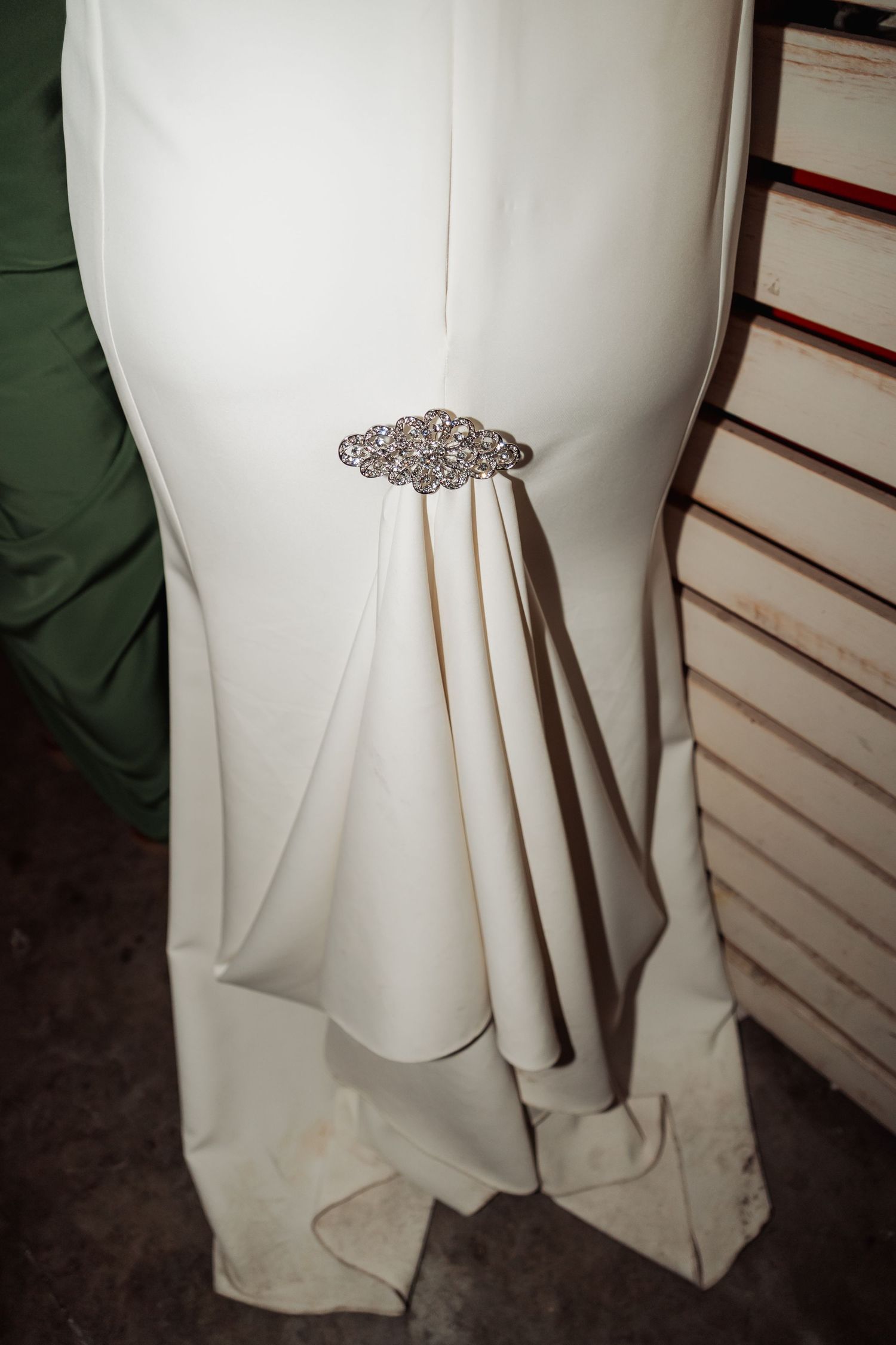 Detail of white wedding dress featuring ornate crystal brooch with draped fabric train.