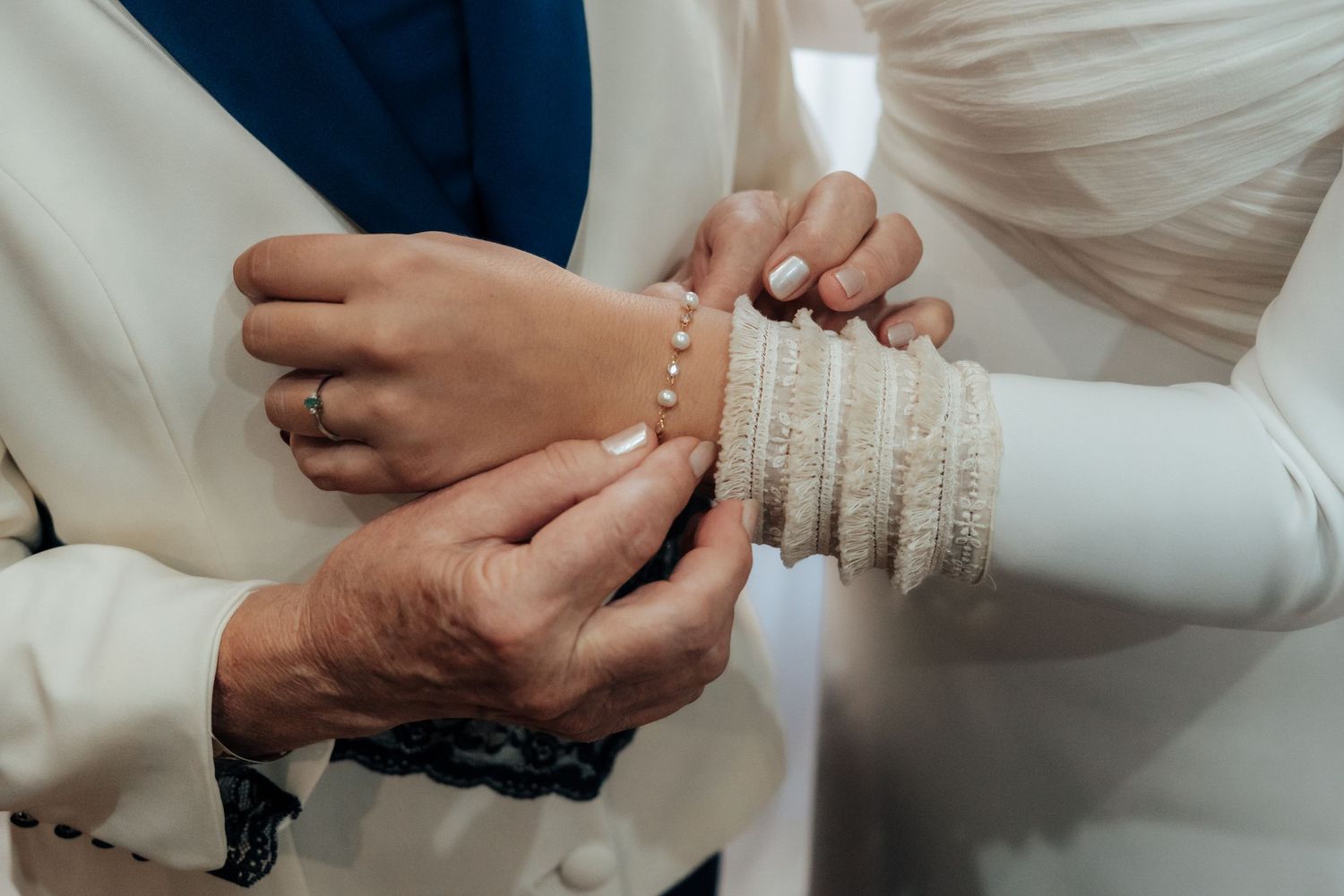 Close-up of hands fastening pearl button cuff on bride's long-sleeved white wedding gown.