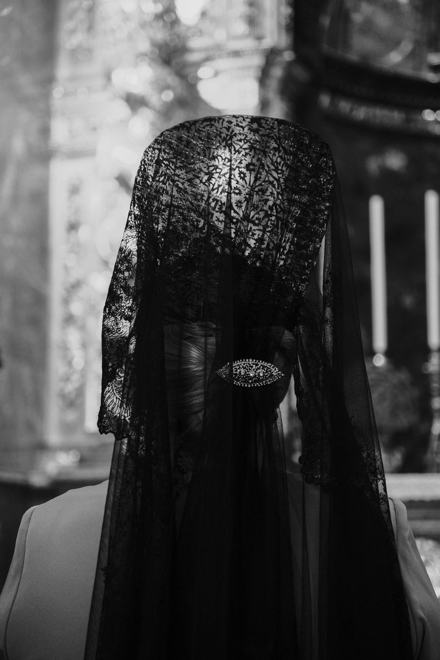 Black and white photo of bride in black lace mantilla veil inside church.