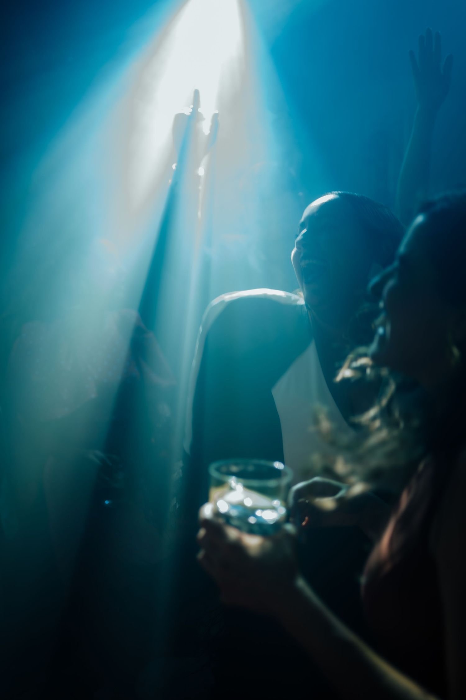 Dramatic silhouette of person holding drink illuminated by blue spotlight beam at party.