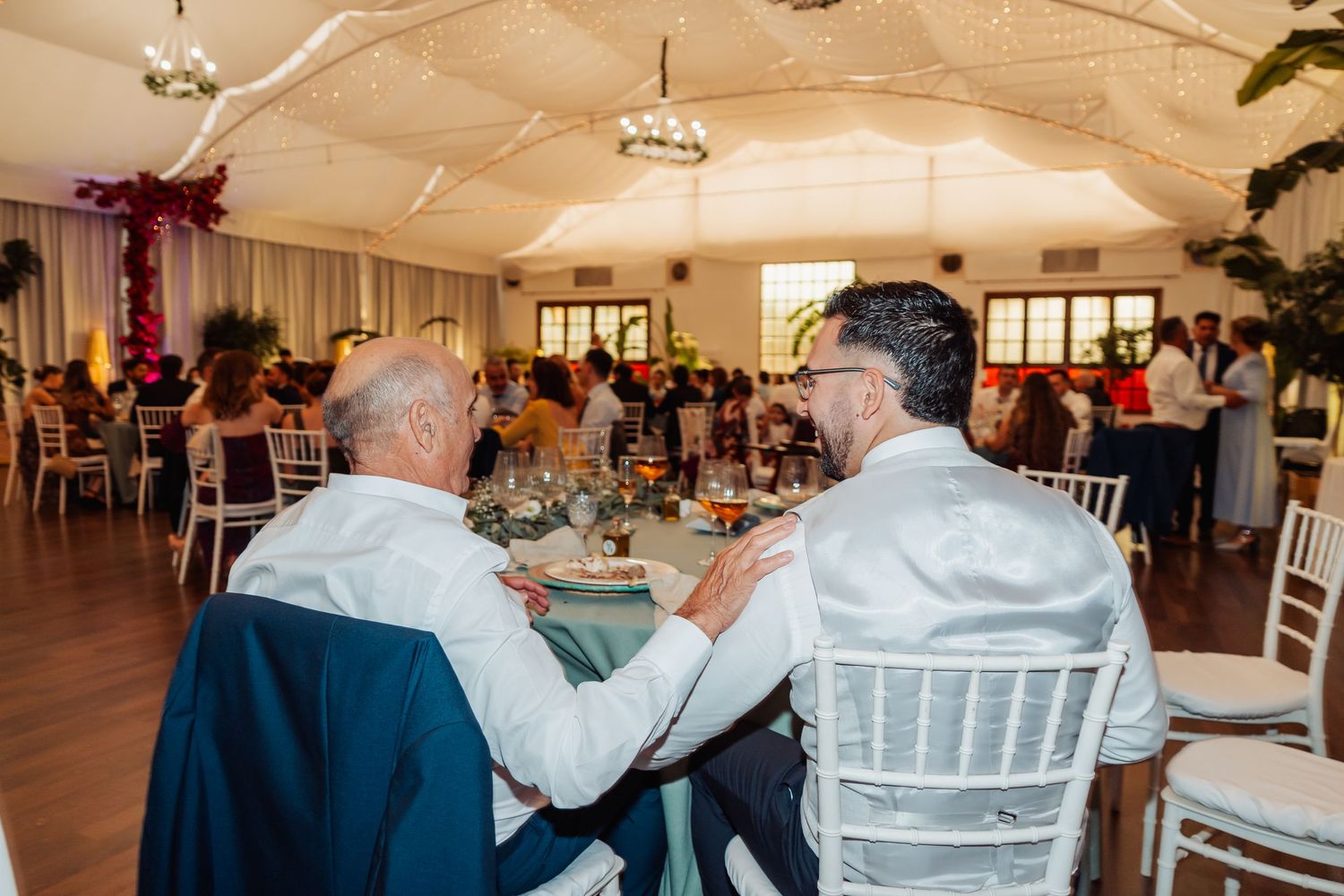 Two male wedding guests sharing an intimate conversation at decorated reception dinner table.