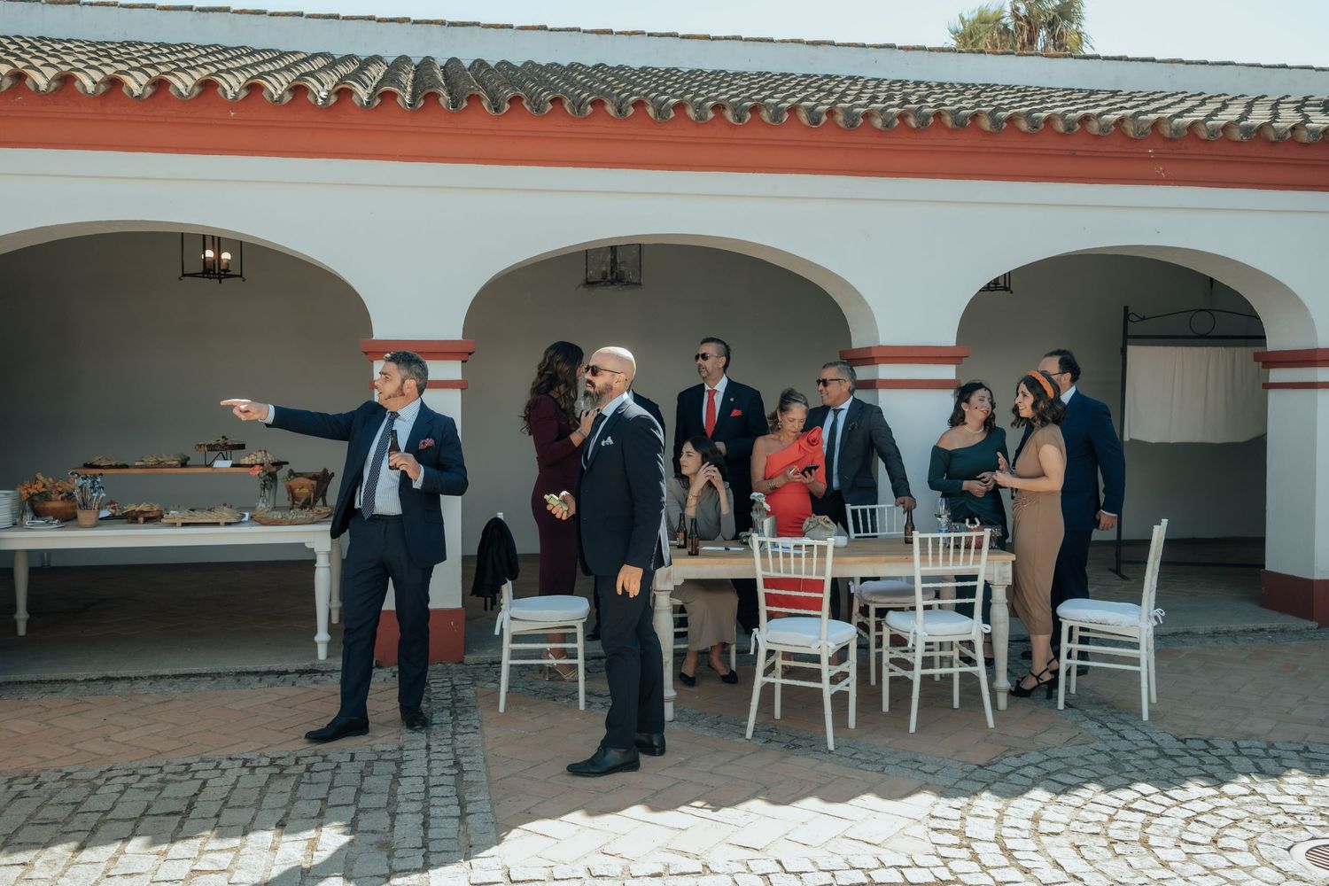 Wedding guests mingle and chat under white arched portico at outdoor Spanish hacienda reception.