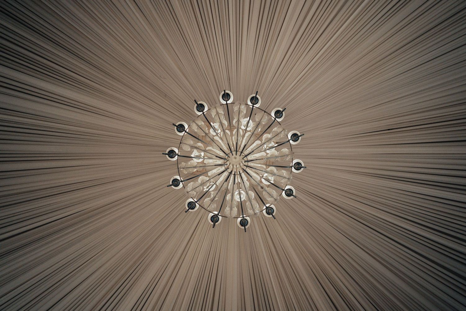 Looking up at an elegant starburst chandelier with crystal accents on a draped ceiling.