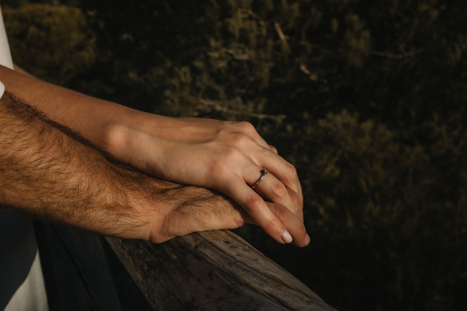 Close-up of engaged couple holding hands on a wooden railing, woman wearing a diamond ring.